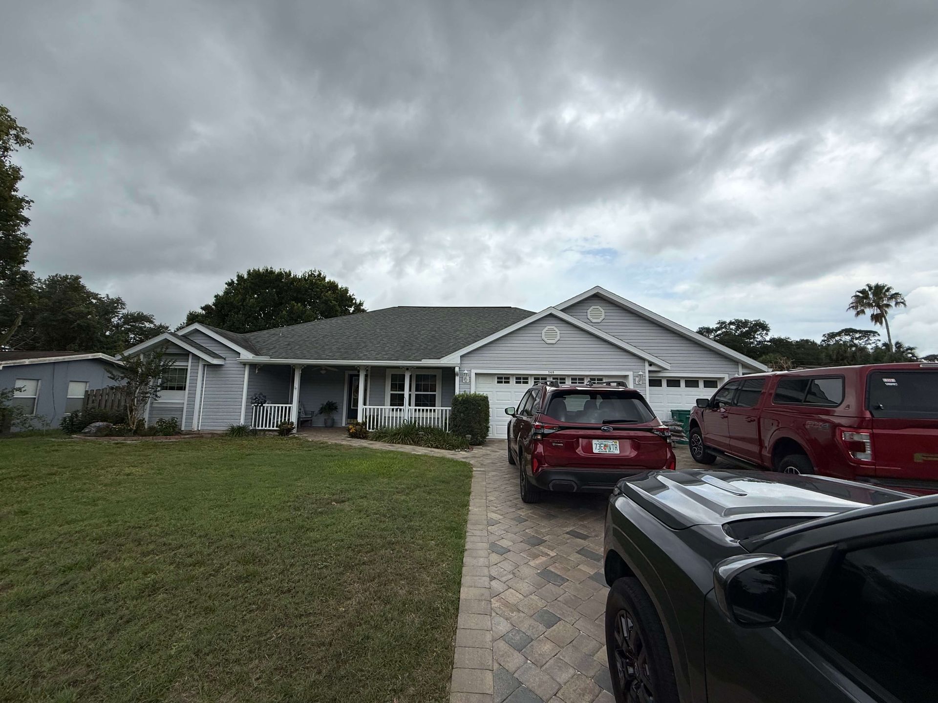 Suburban house with cloudy sky, driveway, and several parked cars in front.