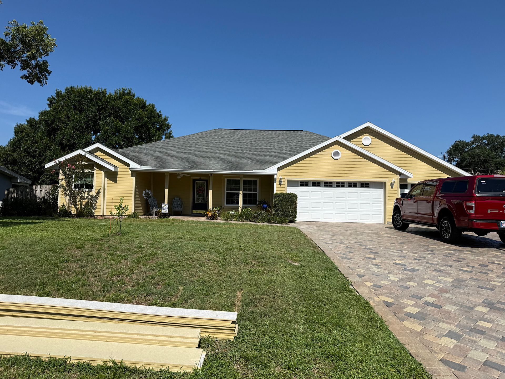 Suburban house with yellow siding, white garage, brick driveway, and a red pickup truck