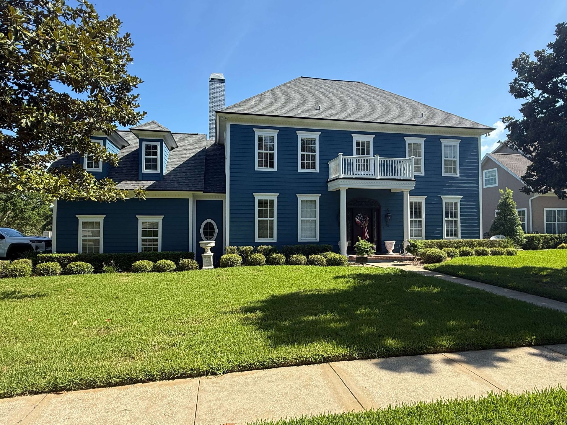Blue two-story house with white trim, front lawn, and sidewalk on a sunny day