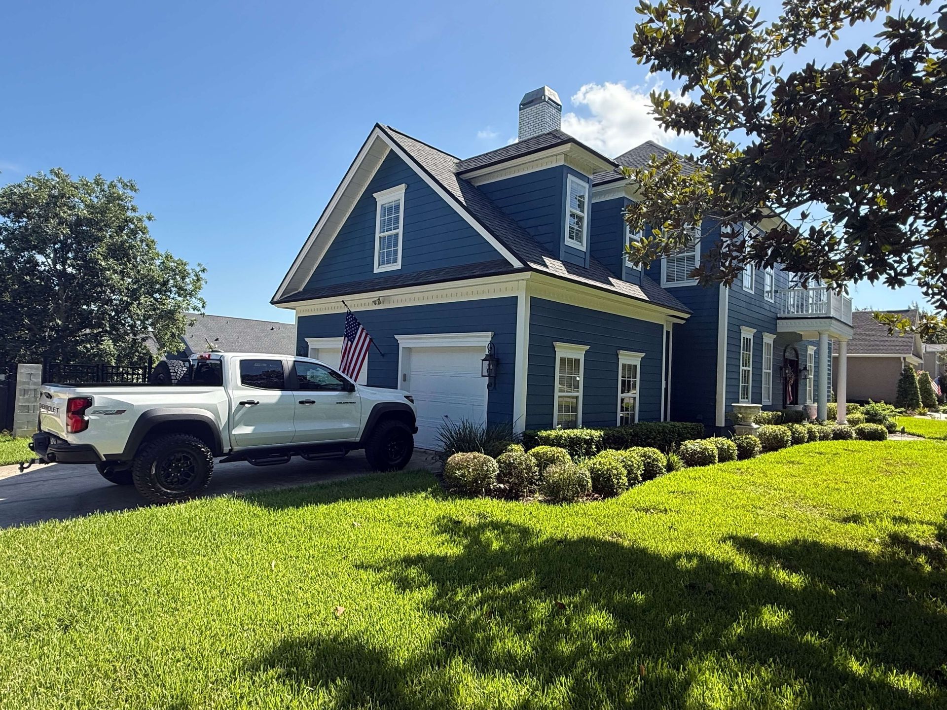 Blue house with white trim and a white pickup truck parked on a sunny lawn.