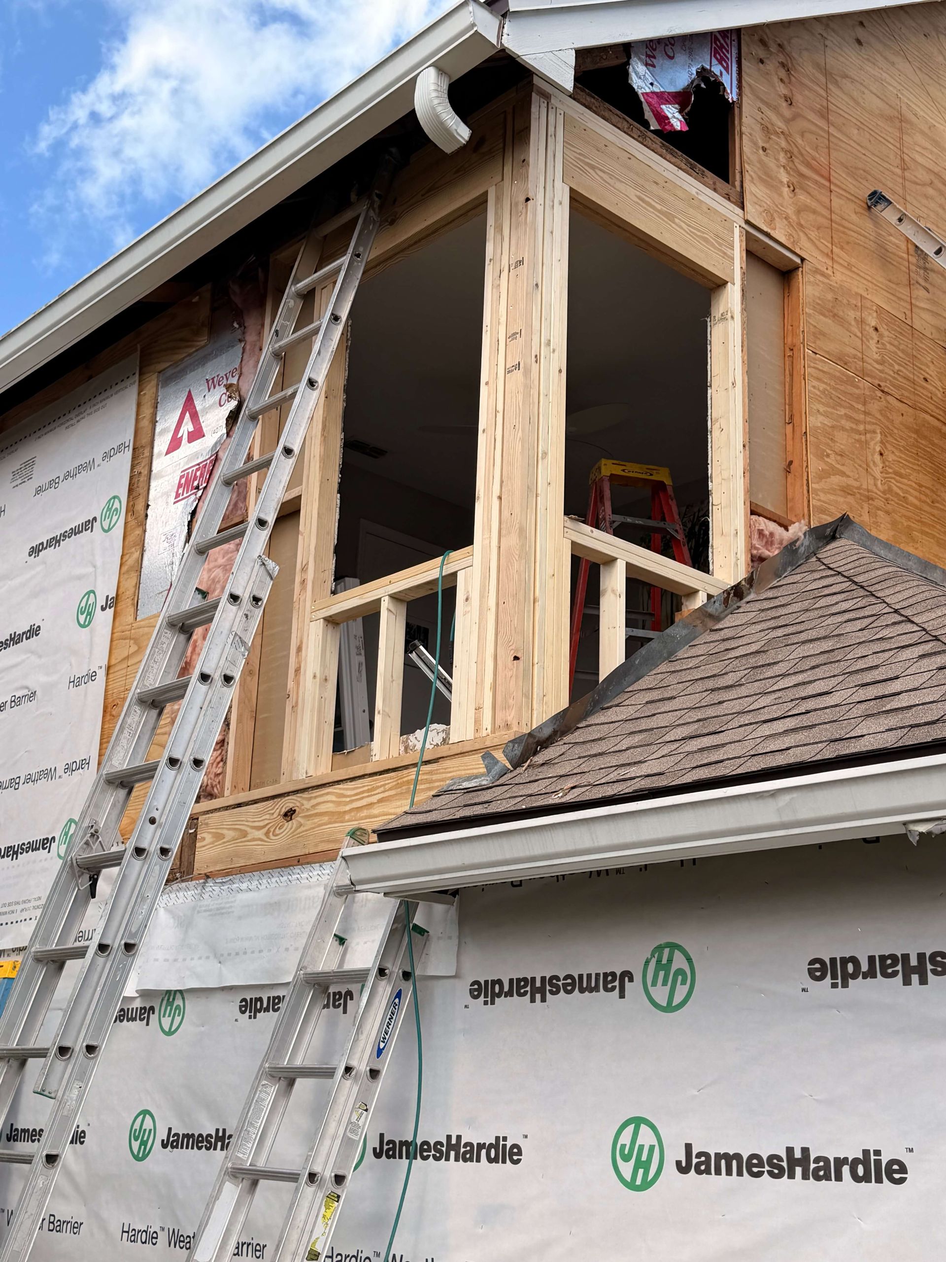 Worker on ladder framing a house addition beside James Hardie siding.