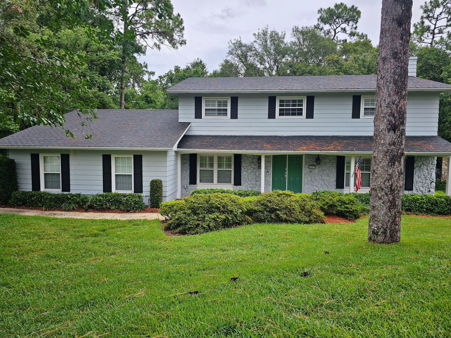 Two-story white suburban house with gray roof and green lawn, partly framed by trees.