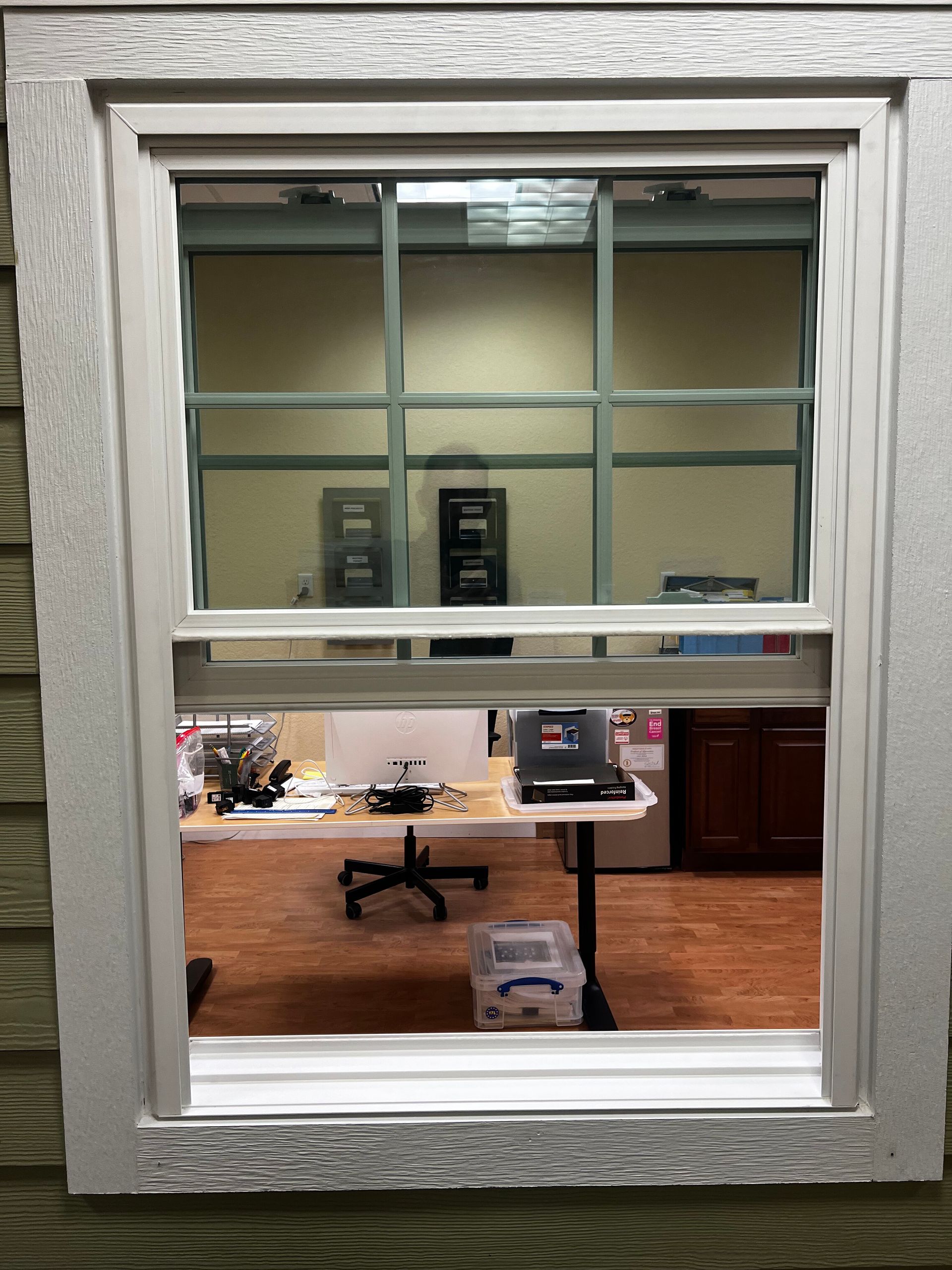 Window into an office with a desk, chair, and fluorescent lights; wood floor visible inside