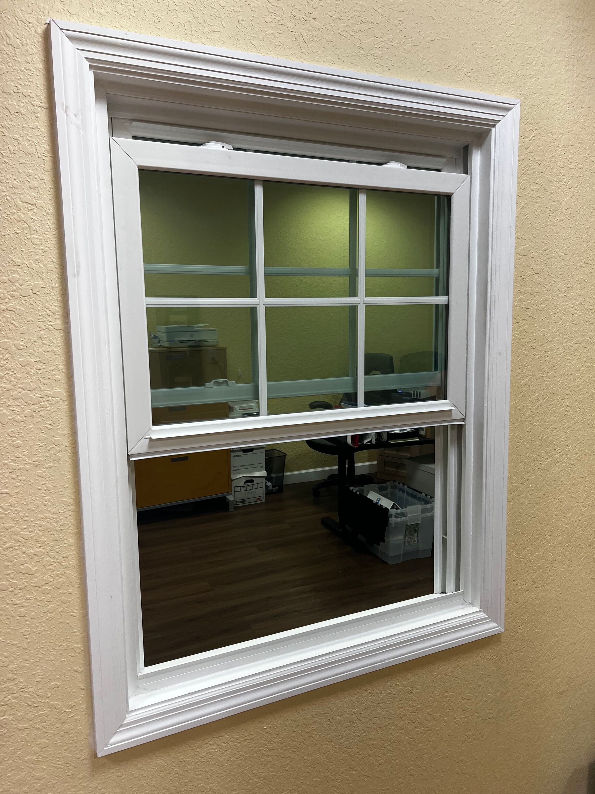 White decorative wall mirror reflecting an office interior with green walls and desk area.