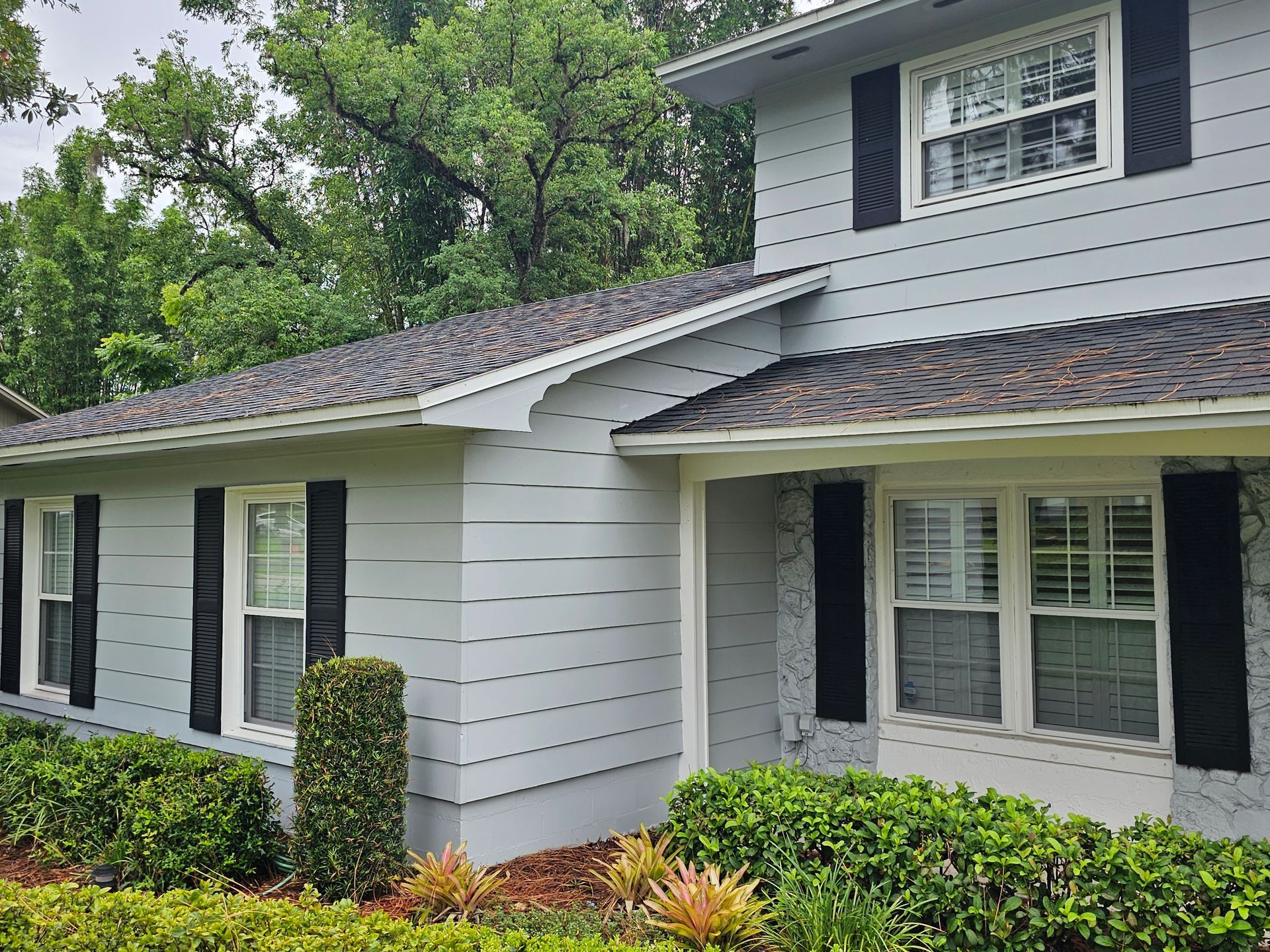 White two-story house with black shutters, dark roof, and green shrubs in front