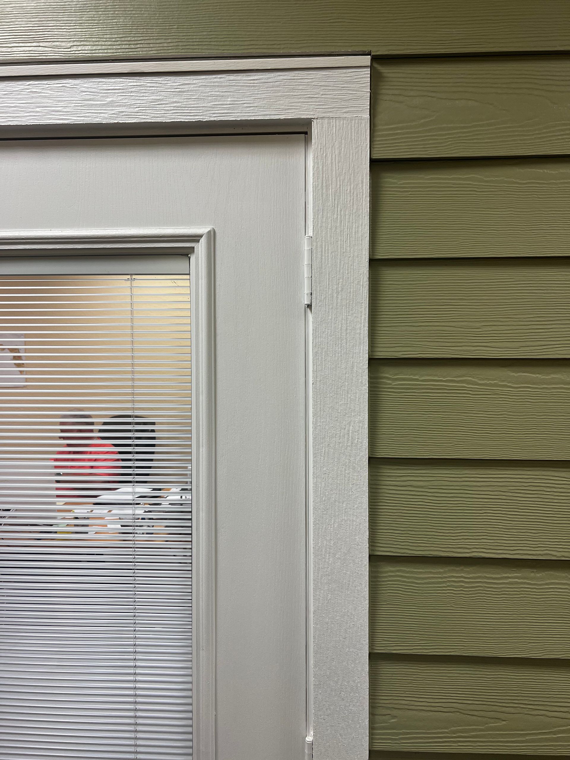 White-framed glass door with blinds beside green exterior siding