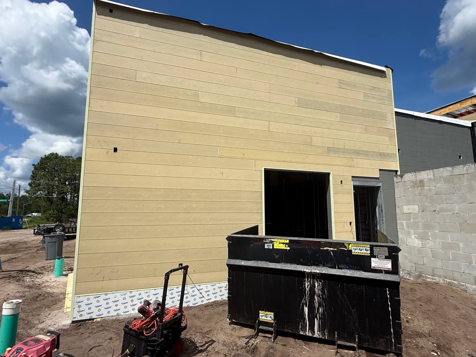 New beige building exterior with open doorway, construction debris, and dumpster in front