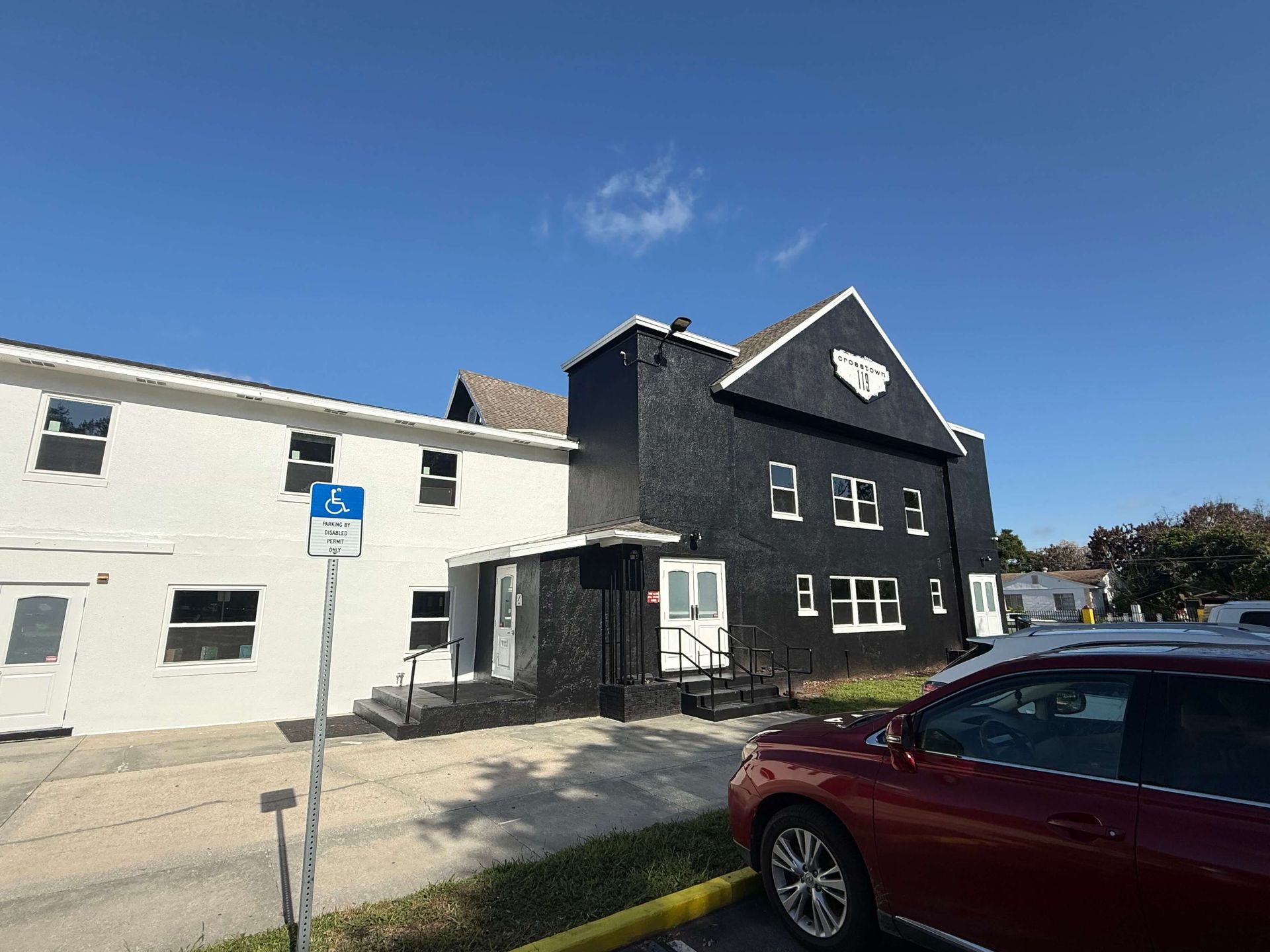 Two-story black-and-white building under a clear blue sky, with a red car parked in front.
