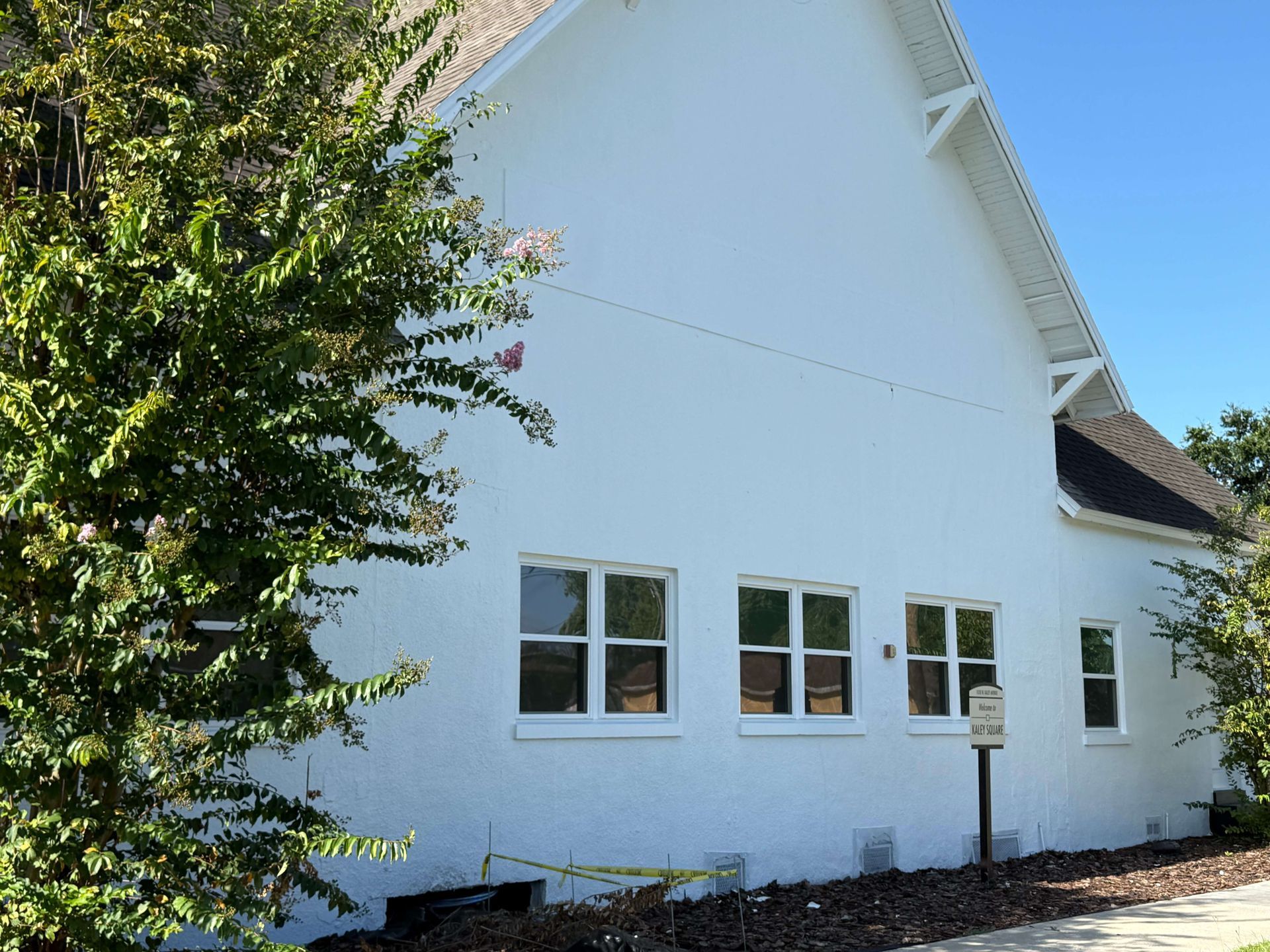 White house exterior with a steep roof, several windows, and a leafy tree in front