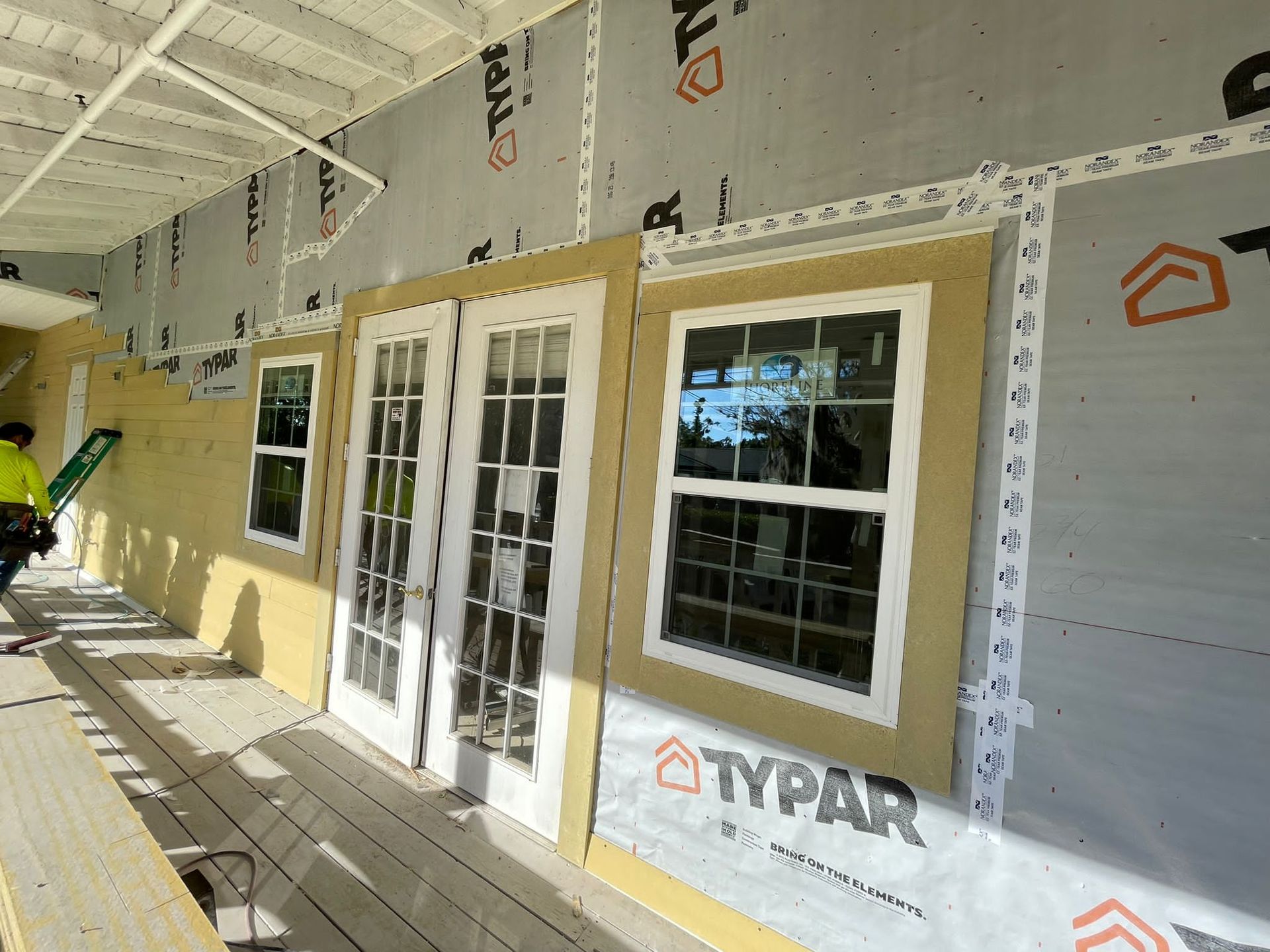 Partially built house exterior with white French doors, windows, and Typar house wrap under a covered porch