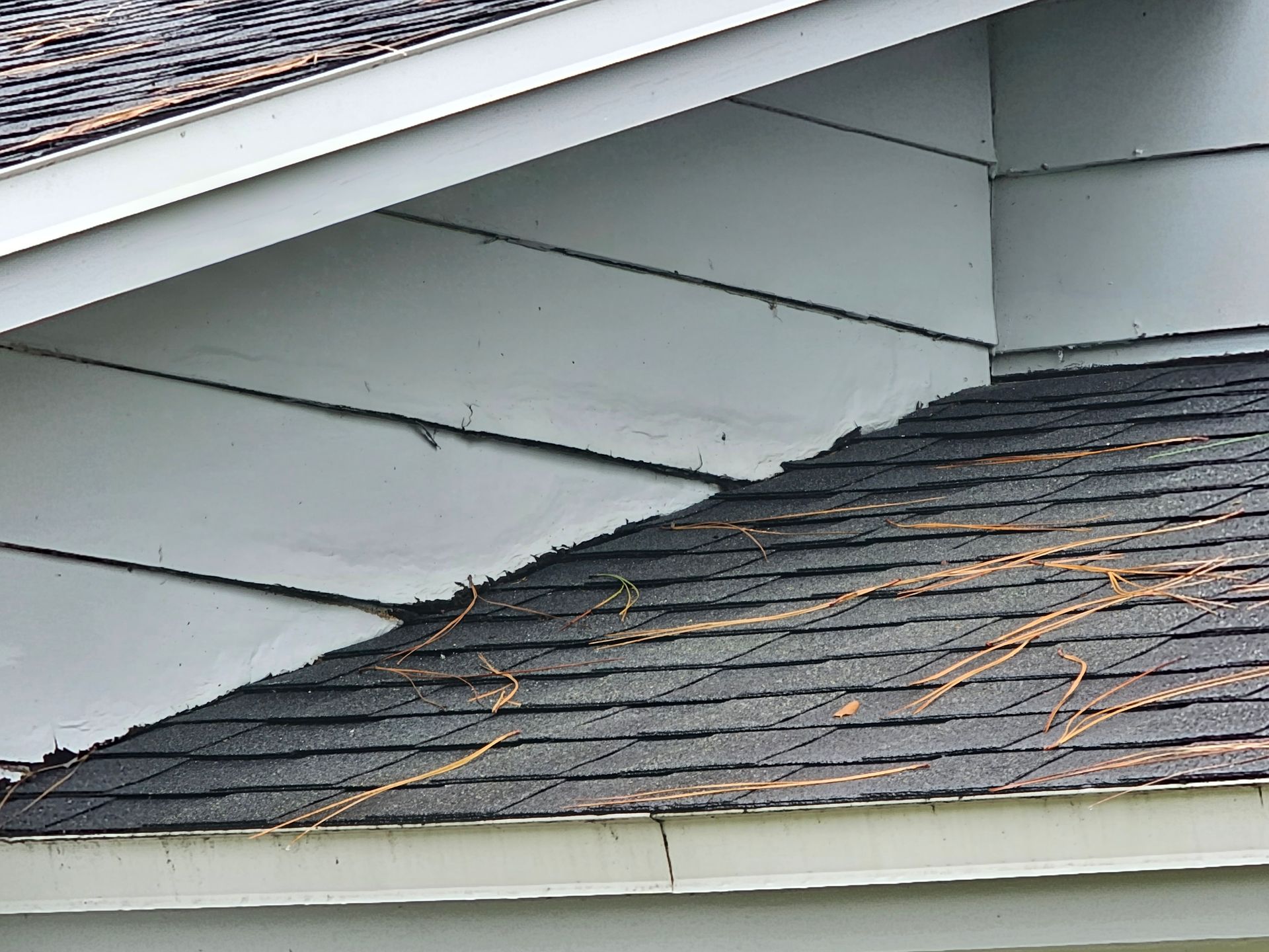 Damaged roof shingles with white soffit panels and a visible gap under the eave