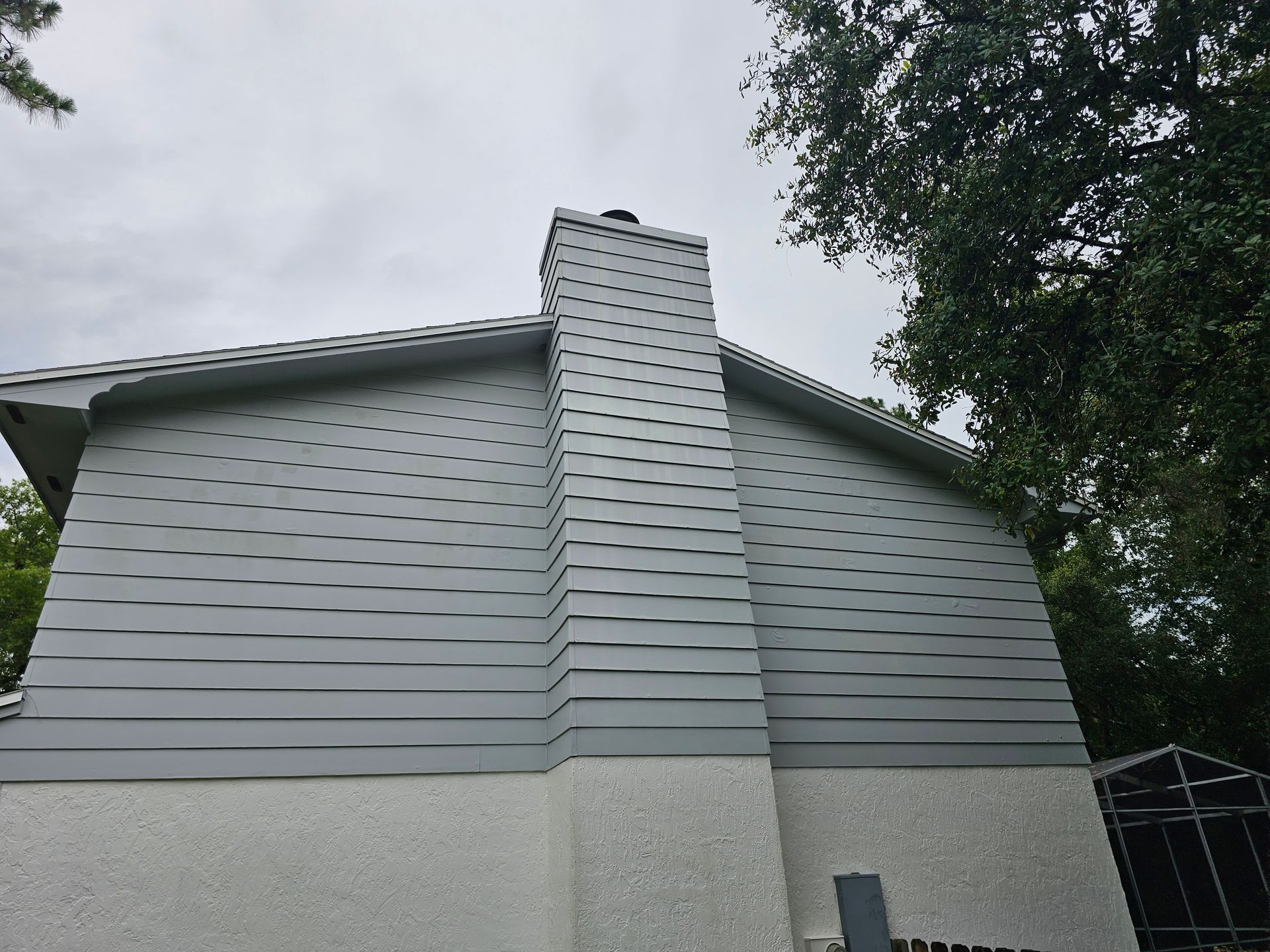 Gray house exterior with a central chimney and trees overhead