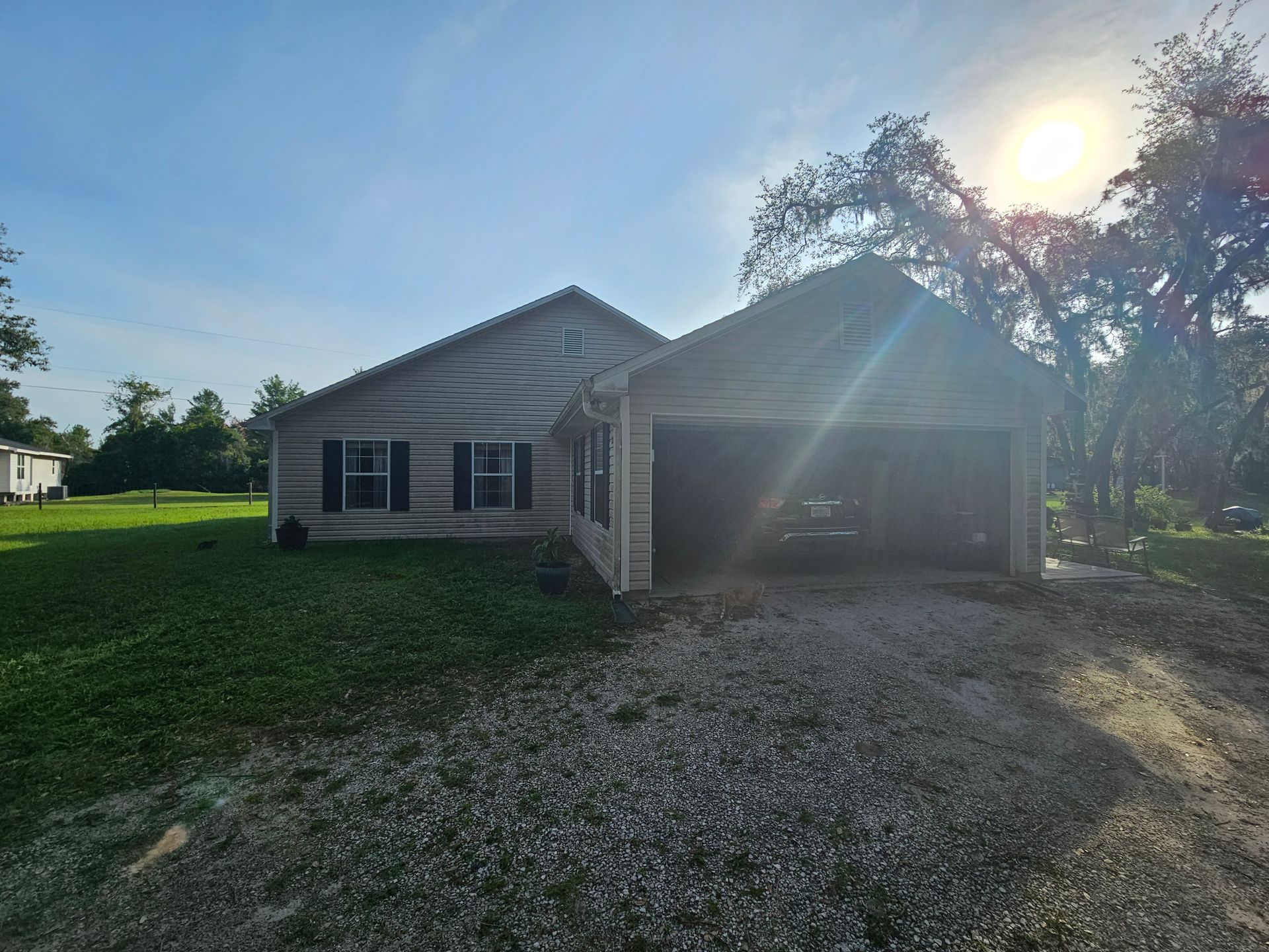 Single-story house with attached garage, gravel driveway, and sun glare in front yard.