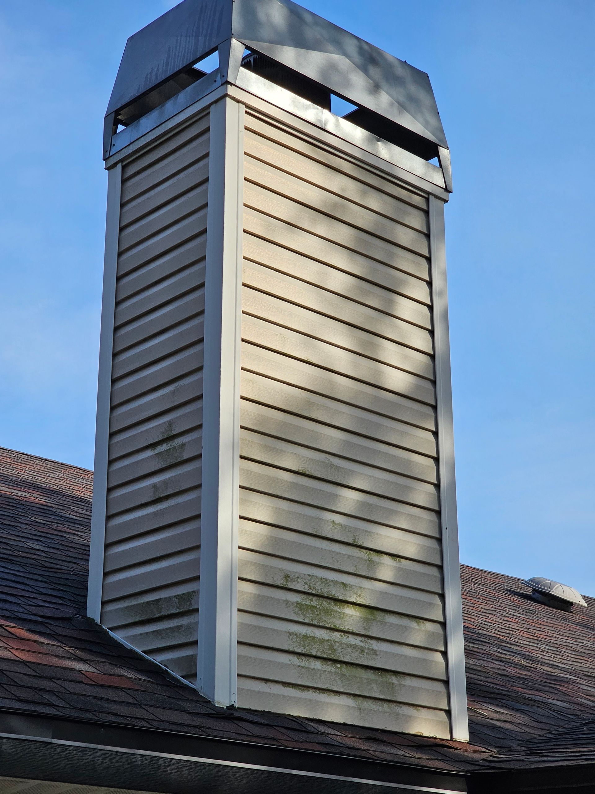 Metal chimney vent on a tiled roof against a blue sky