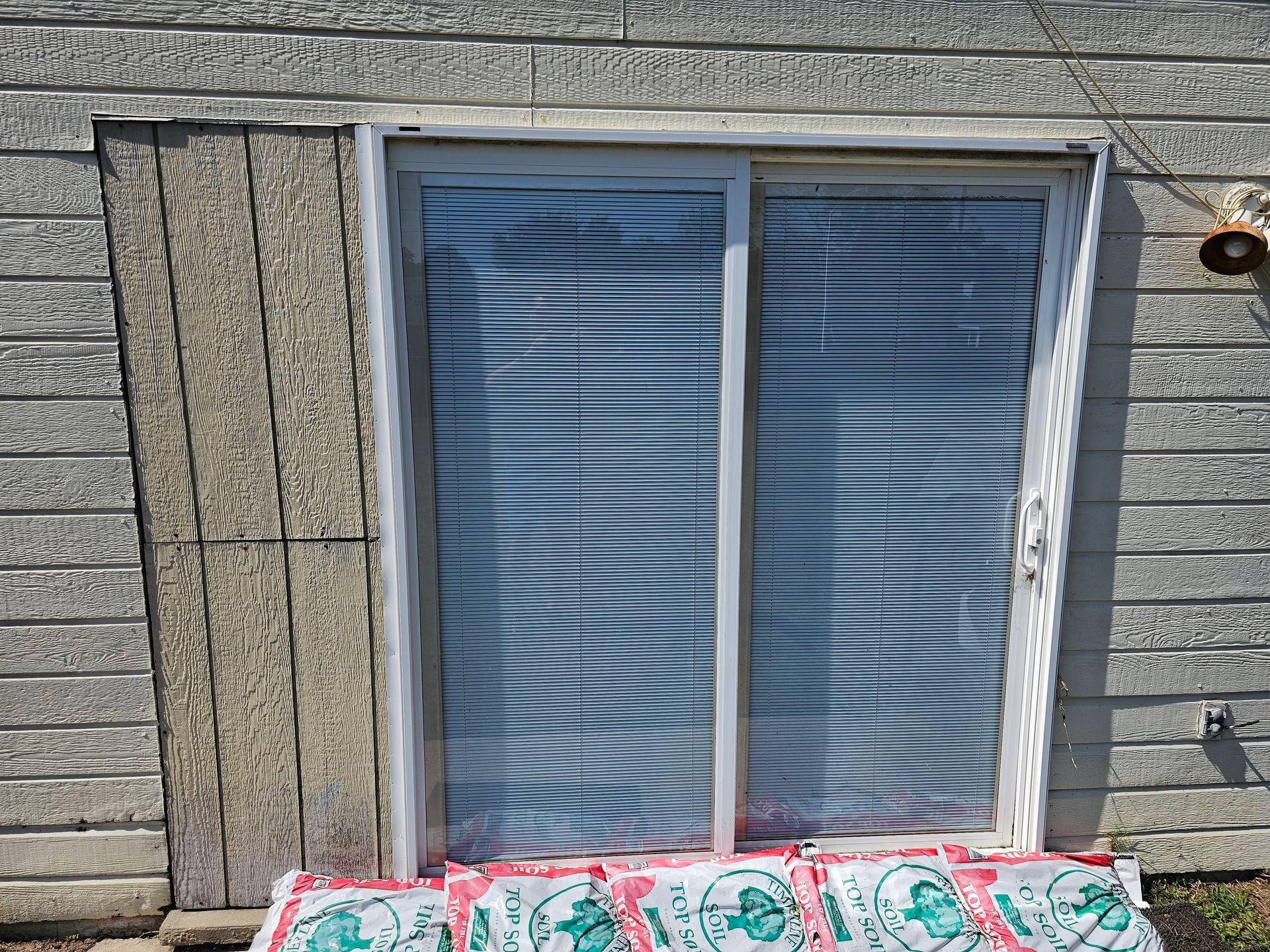 Blue window with closed blinds in a gray stone wall, with colorful flowers at the bottom