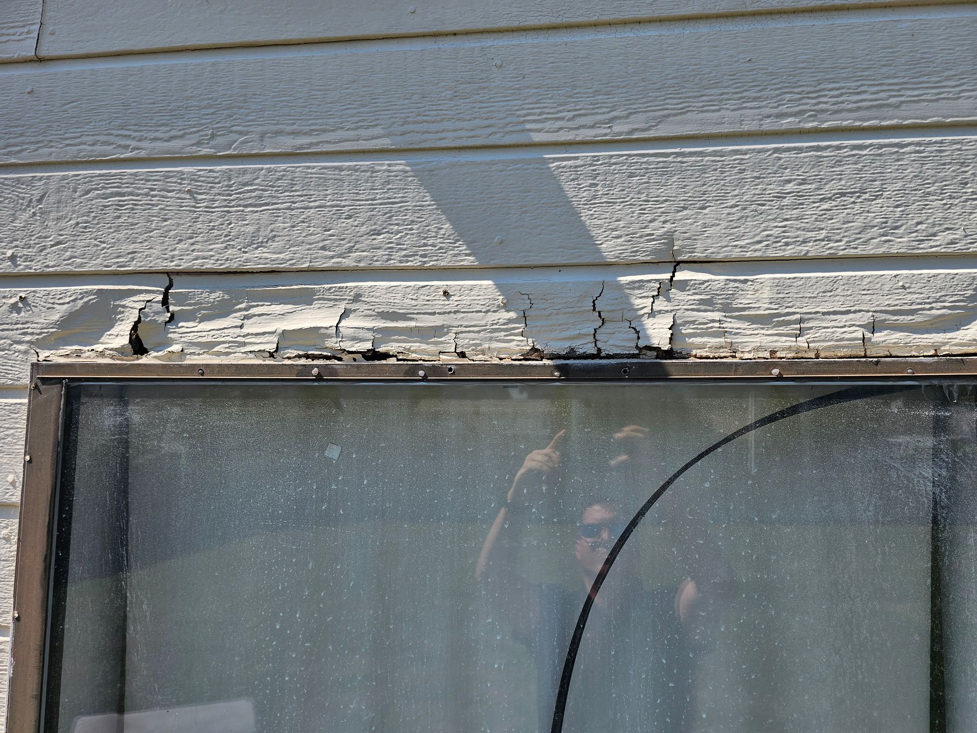 Damaged wooden exterior wall above a window with peeling paint and cracked trim