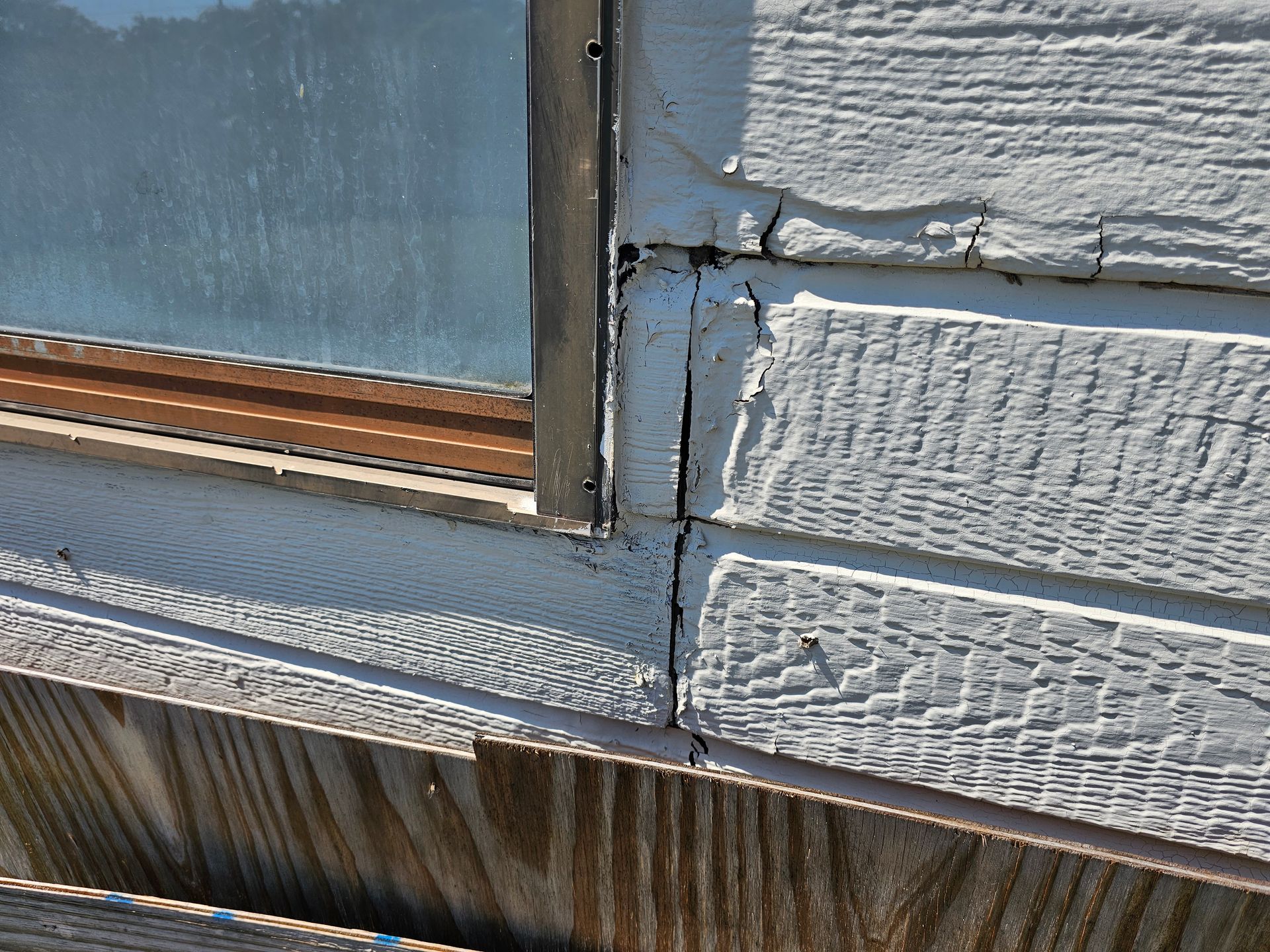 Close-up of weathered house siding with peeling paint and cracked trim around a window