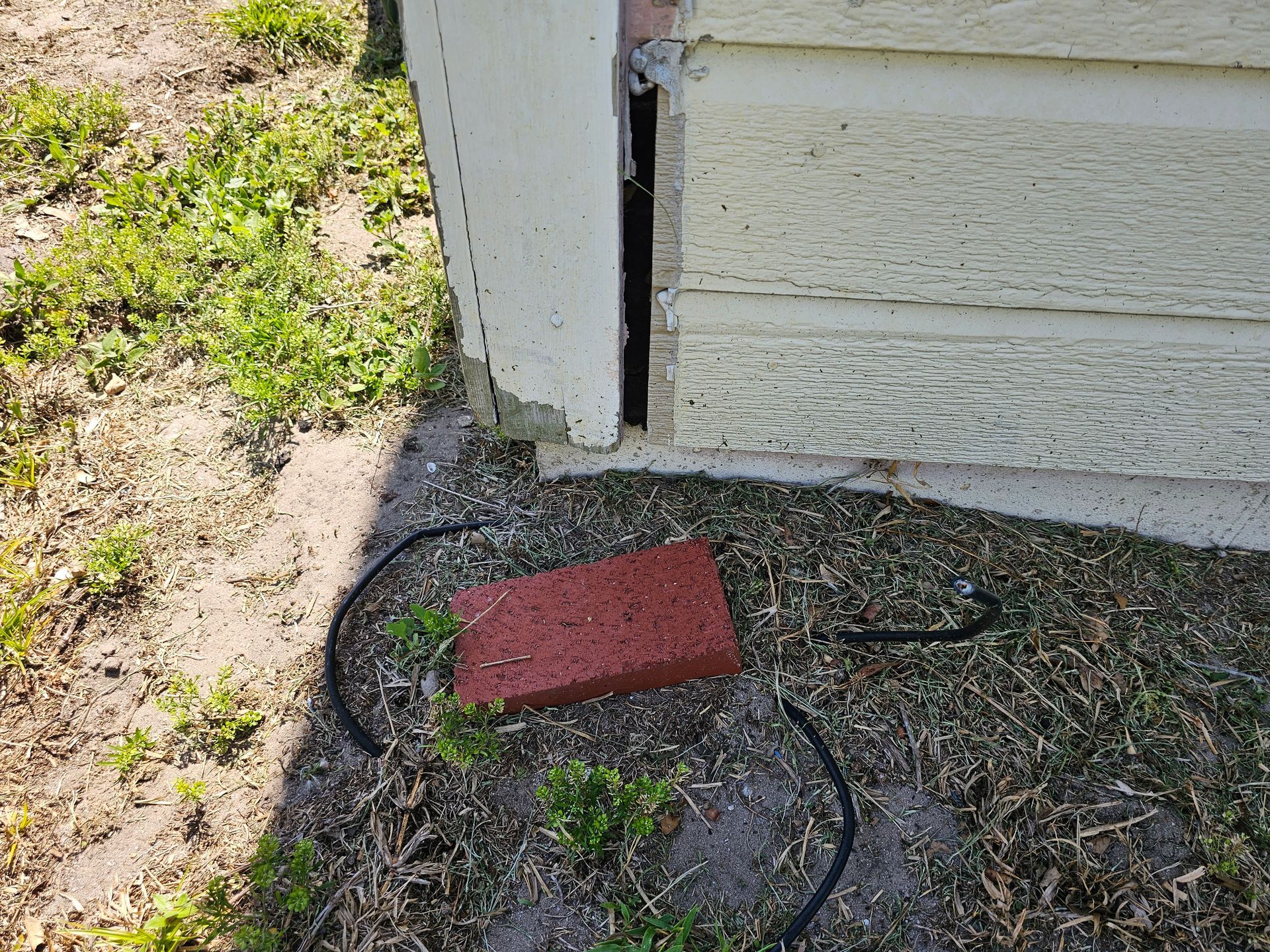 Red brick and black cable on gravel beside a white building corner with grass nearby