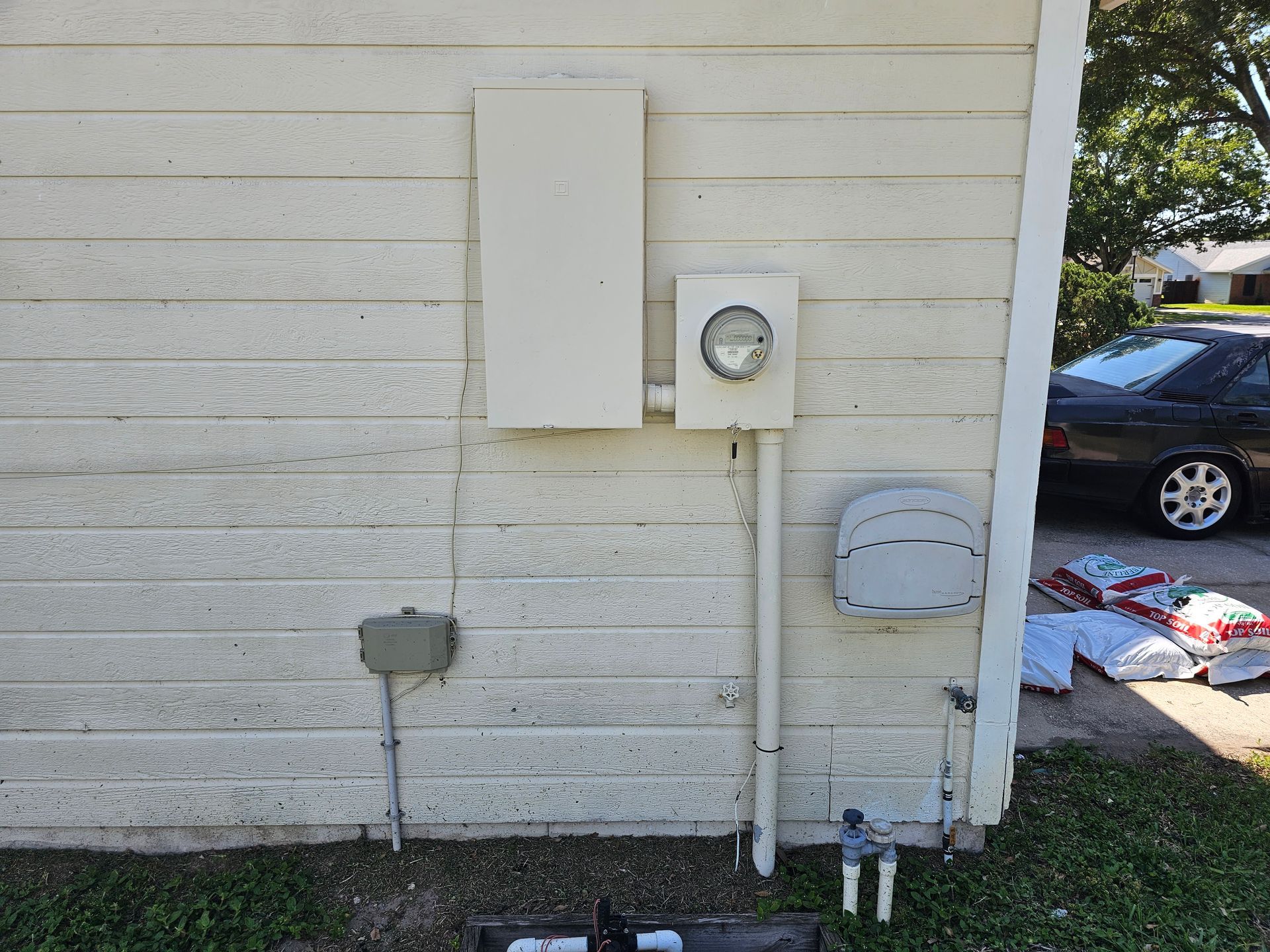 Side of a house with utility boxes, meter, conduit, and a parked car in the background