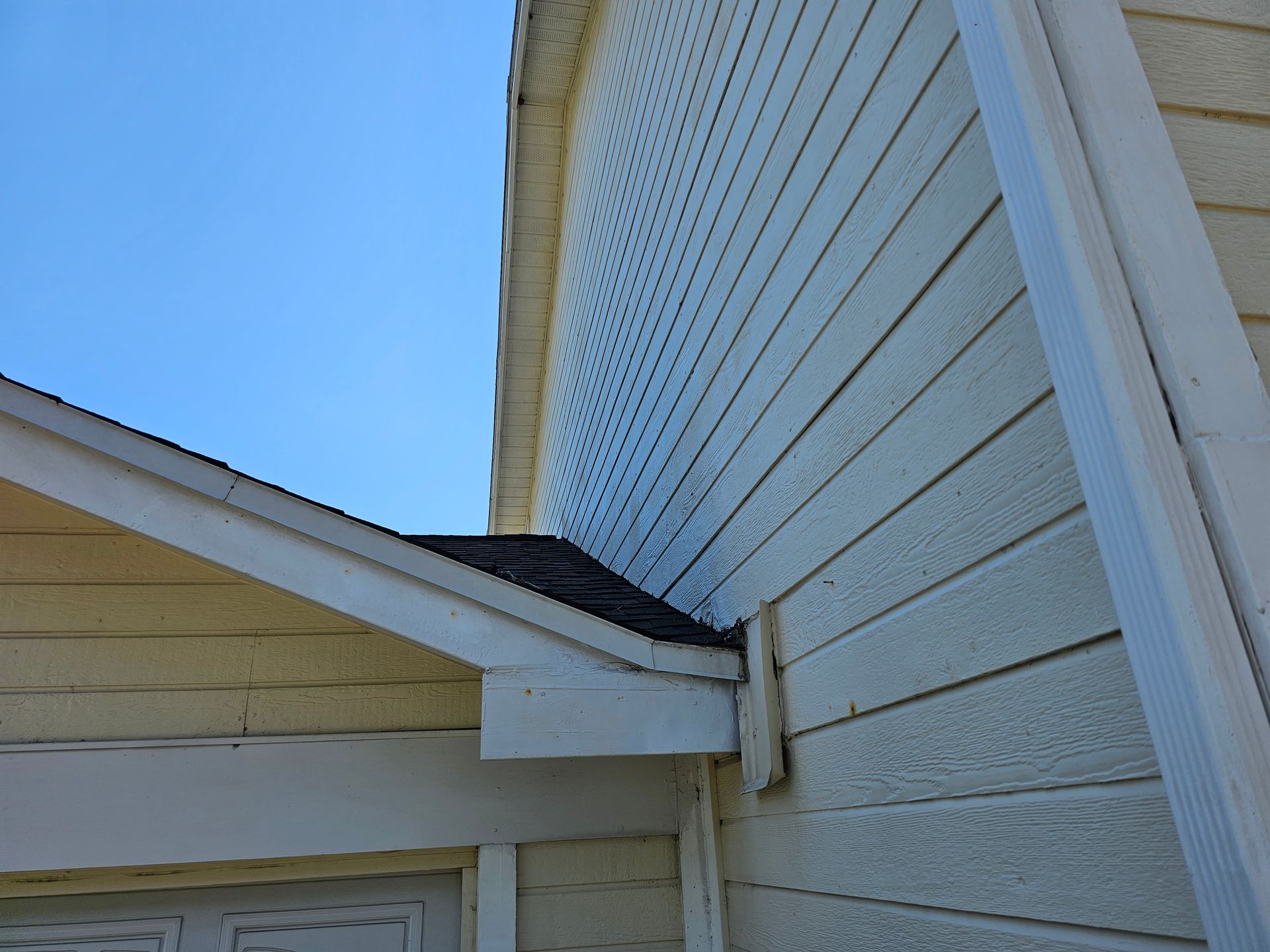 White house exterior with a sloped roof meeting vertical siding under a blue sky