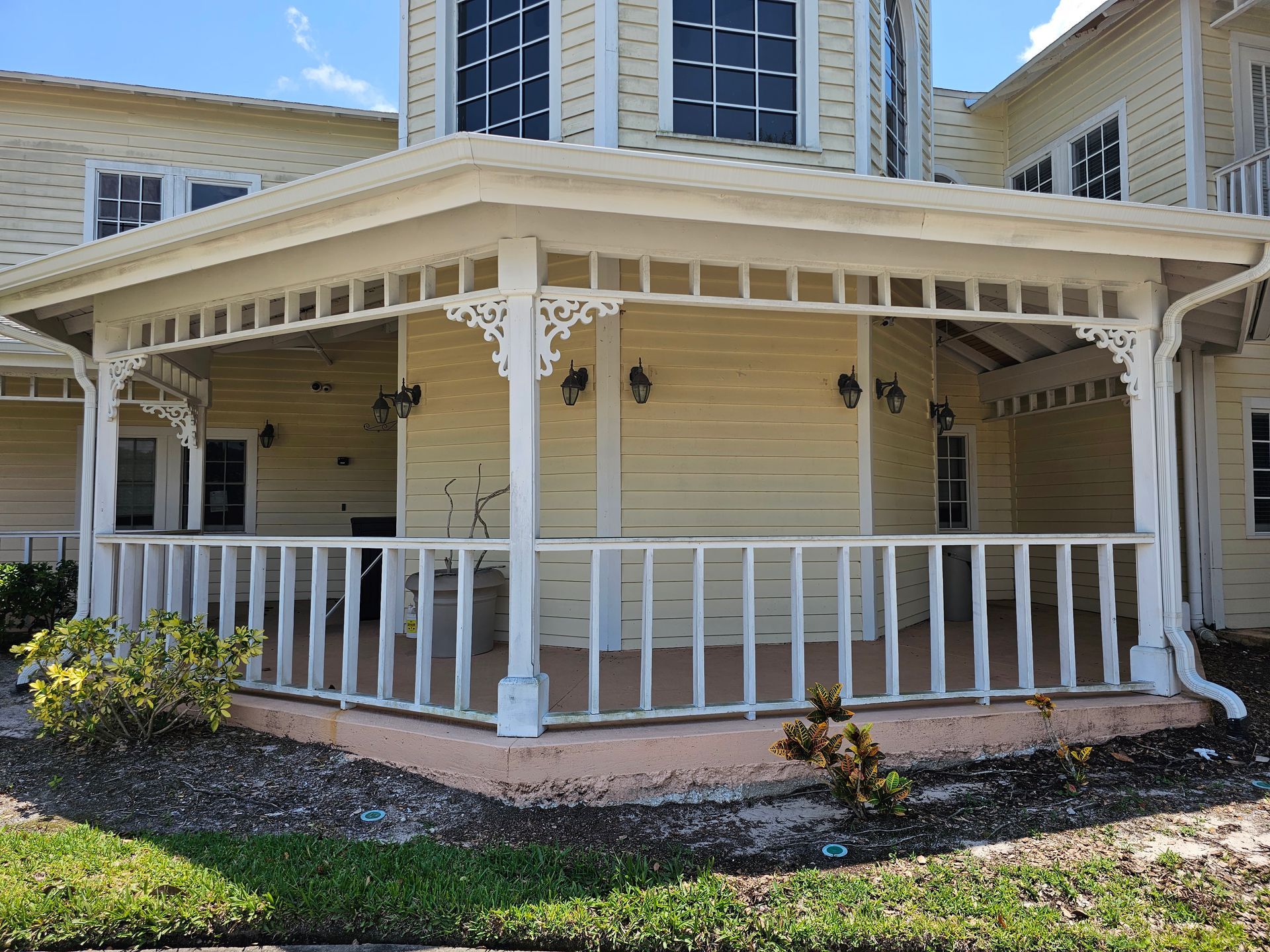 White wraparound porch with railings on a beige house in a residential neighborhood