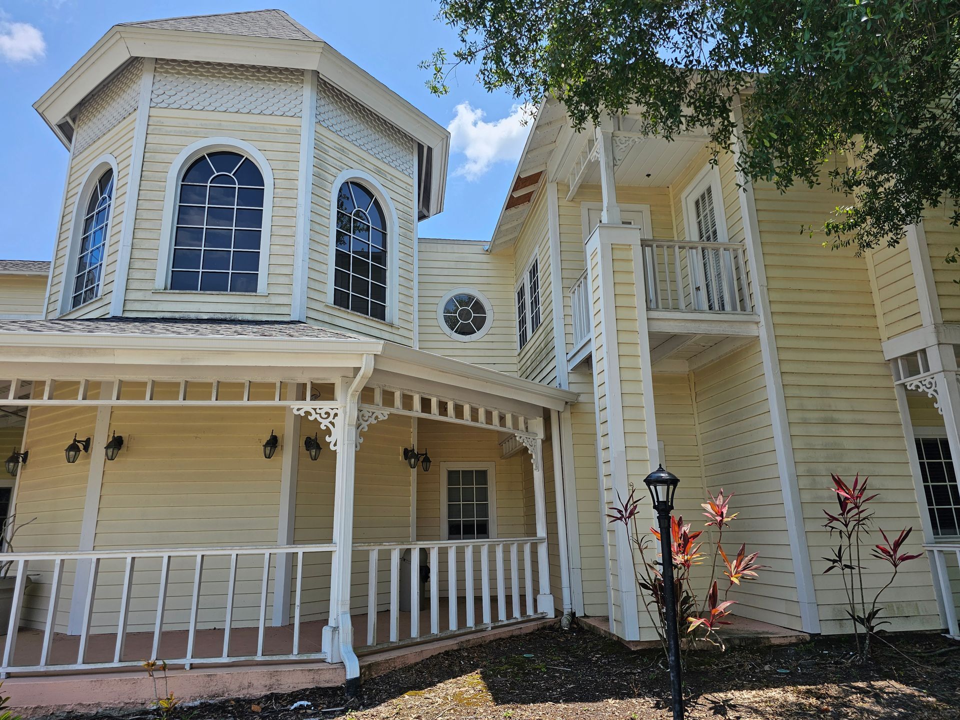 Victorian-style cream house with octagonal turret, wraparound porch, and white trim under a blue sky