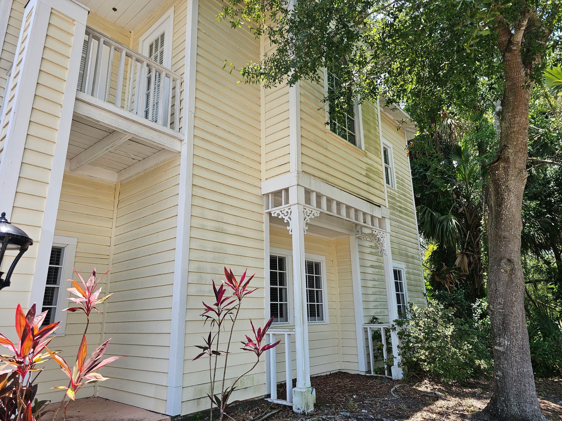 Yellow house exterior with white trim, balconies, and trees in front