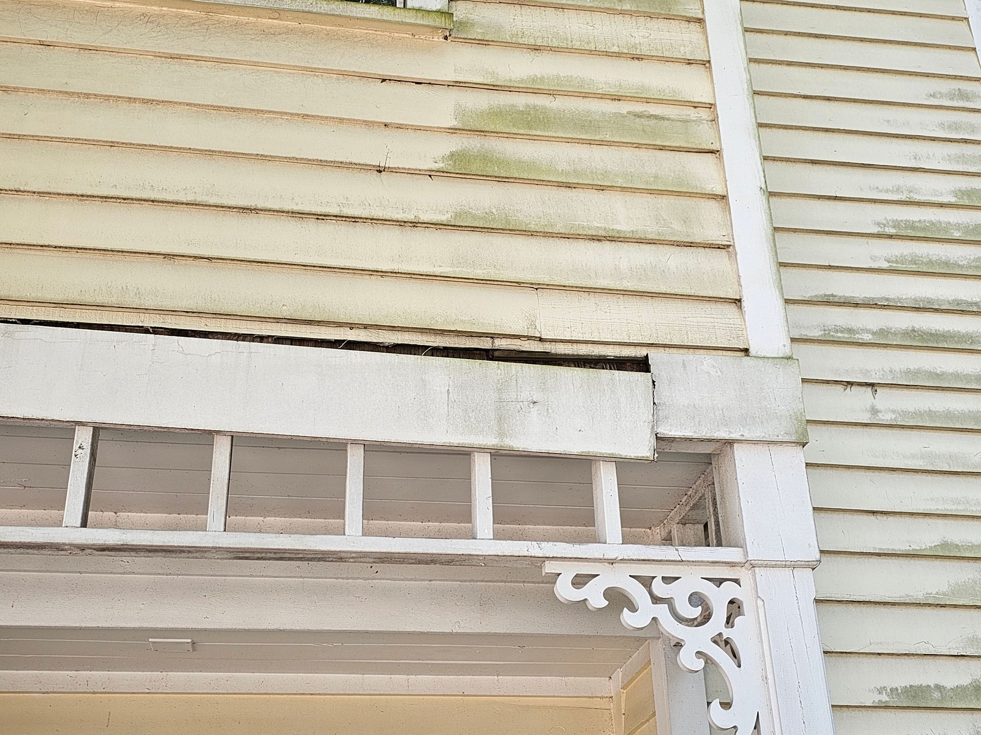 Close-up of a weathered beige window blind with white trim and decorative porch trim beneath it