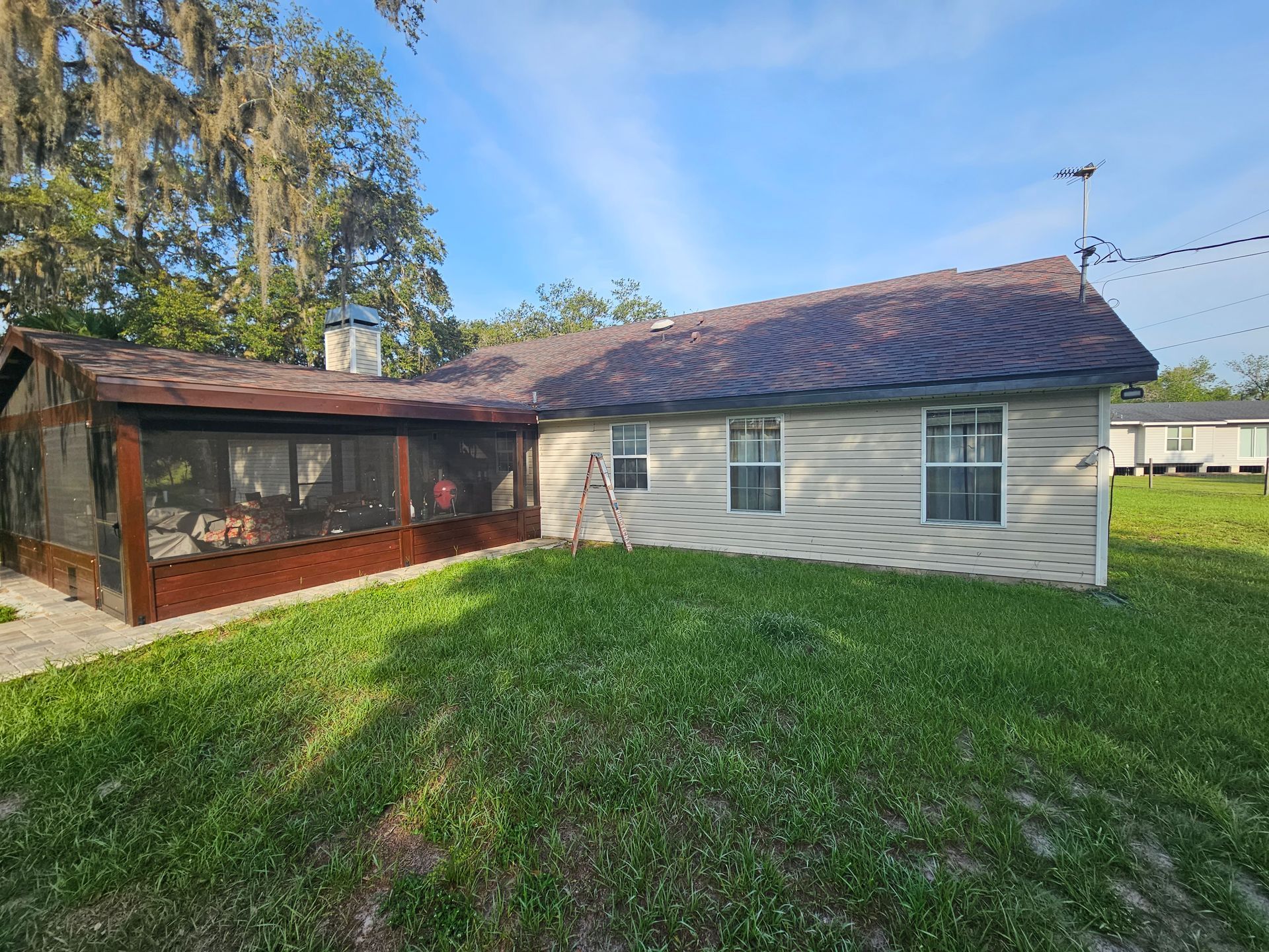 Single-story house with screened porch, white siding, and a red-tiled roof on a grassy yard
