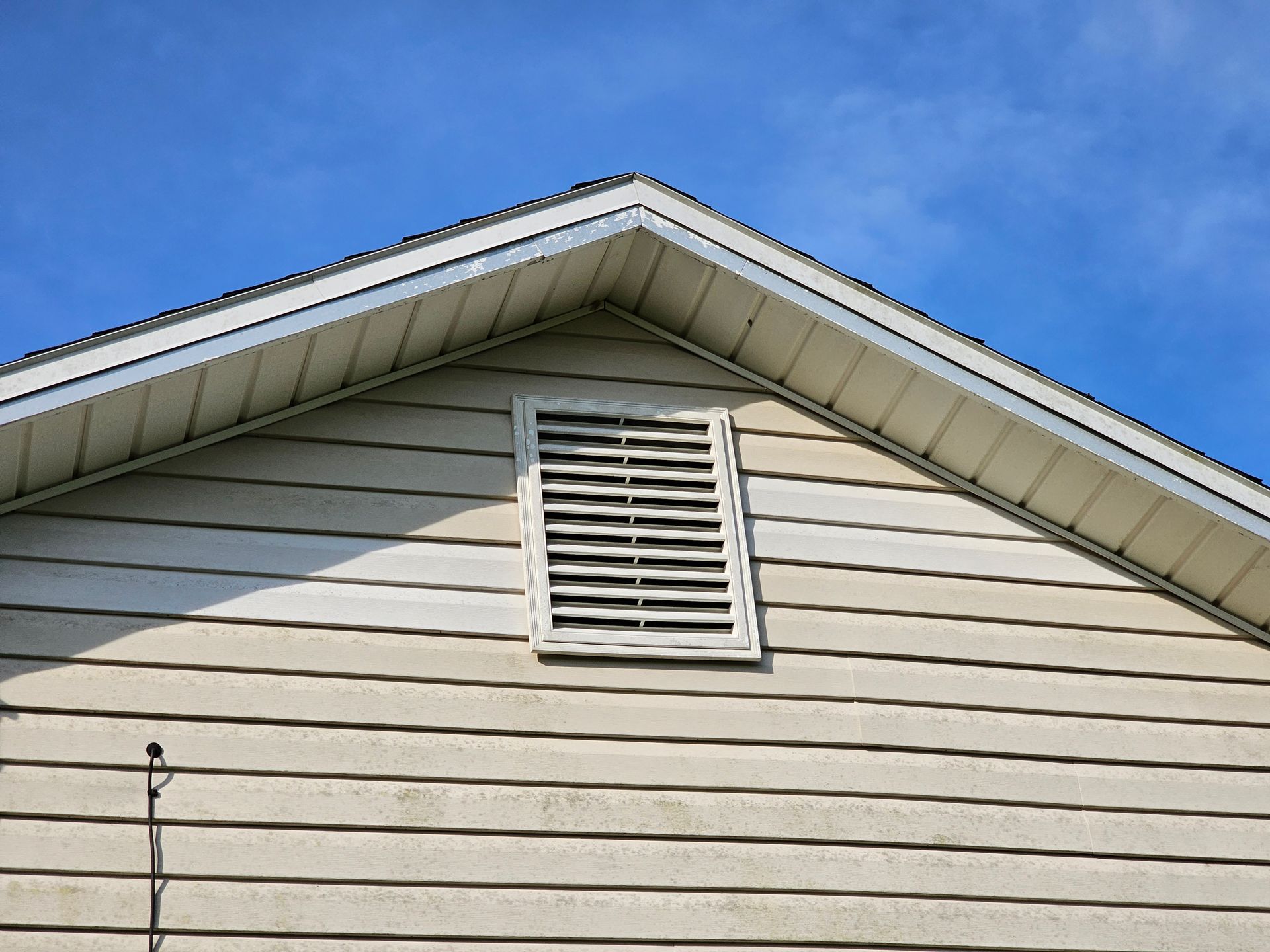 White house gable with beige siding and a small louvered vent against a blue sky