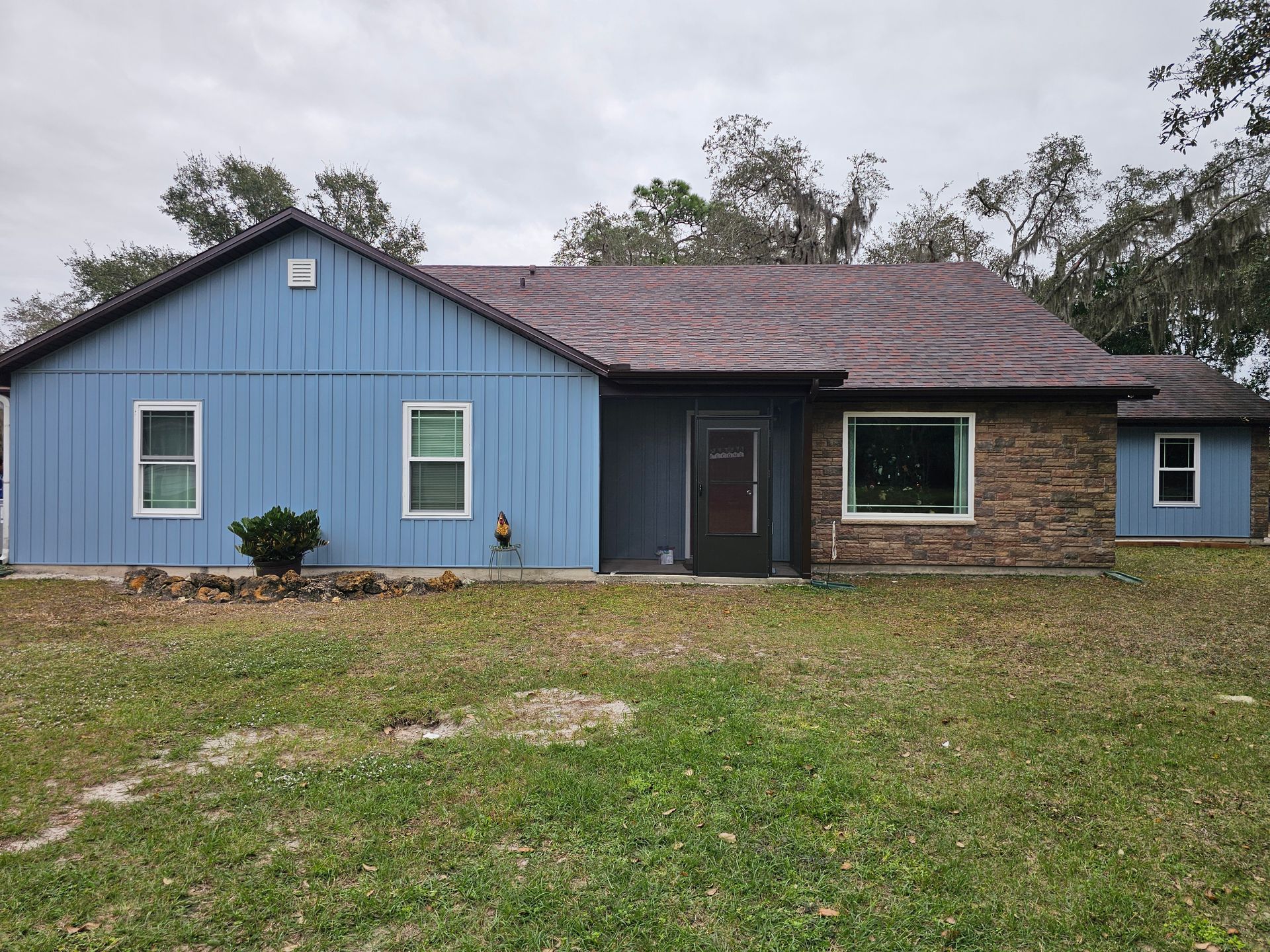 Single-story house with blue siding, brick exterior, and a grassy front yard under cloudy skies