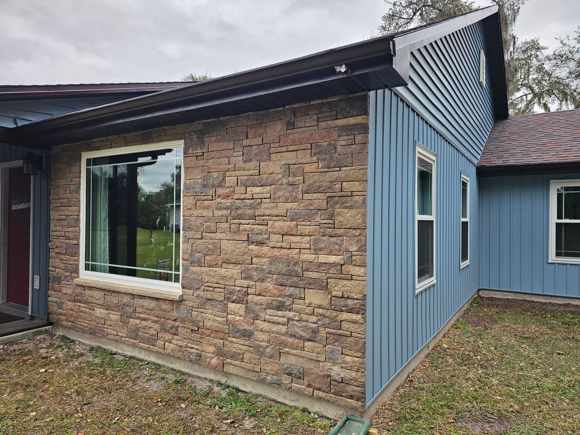 Exterior corner of a house with stone and blue siding, large window, and covered roofline