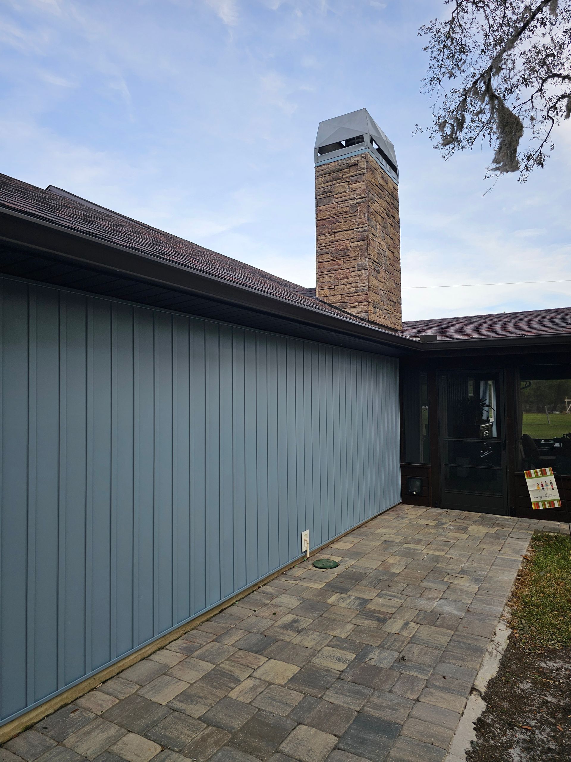 Blue-sided building with a brick chimney and paved courtyard under a cloudy sky