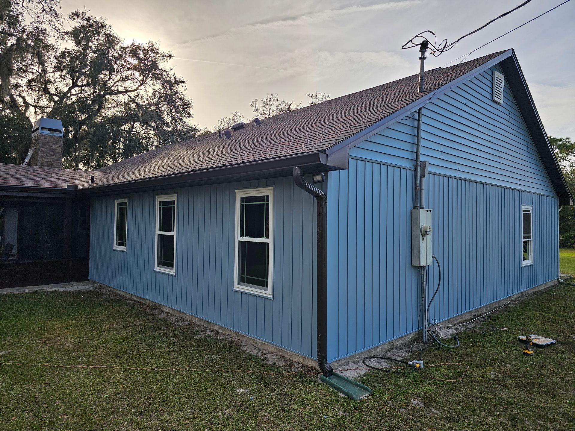 Blue wooden house exterior with white-trimmed windows and a dark roof on a grassy lot.