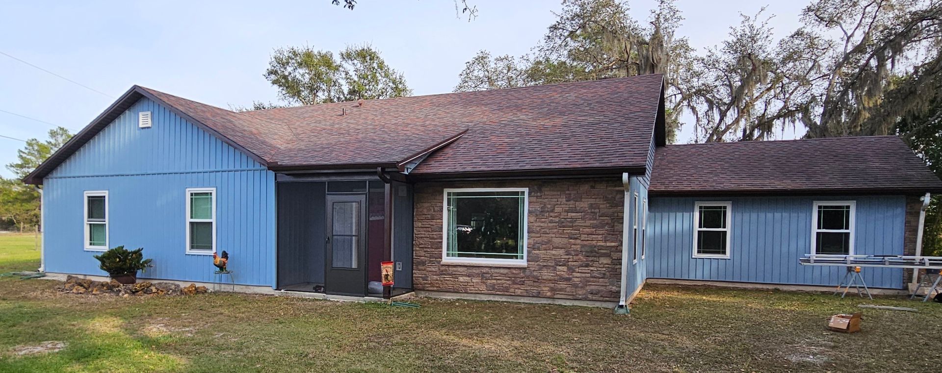 Blue and brown single-story house with a detached blue wing and grassy yard