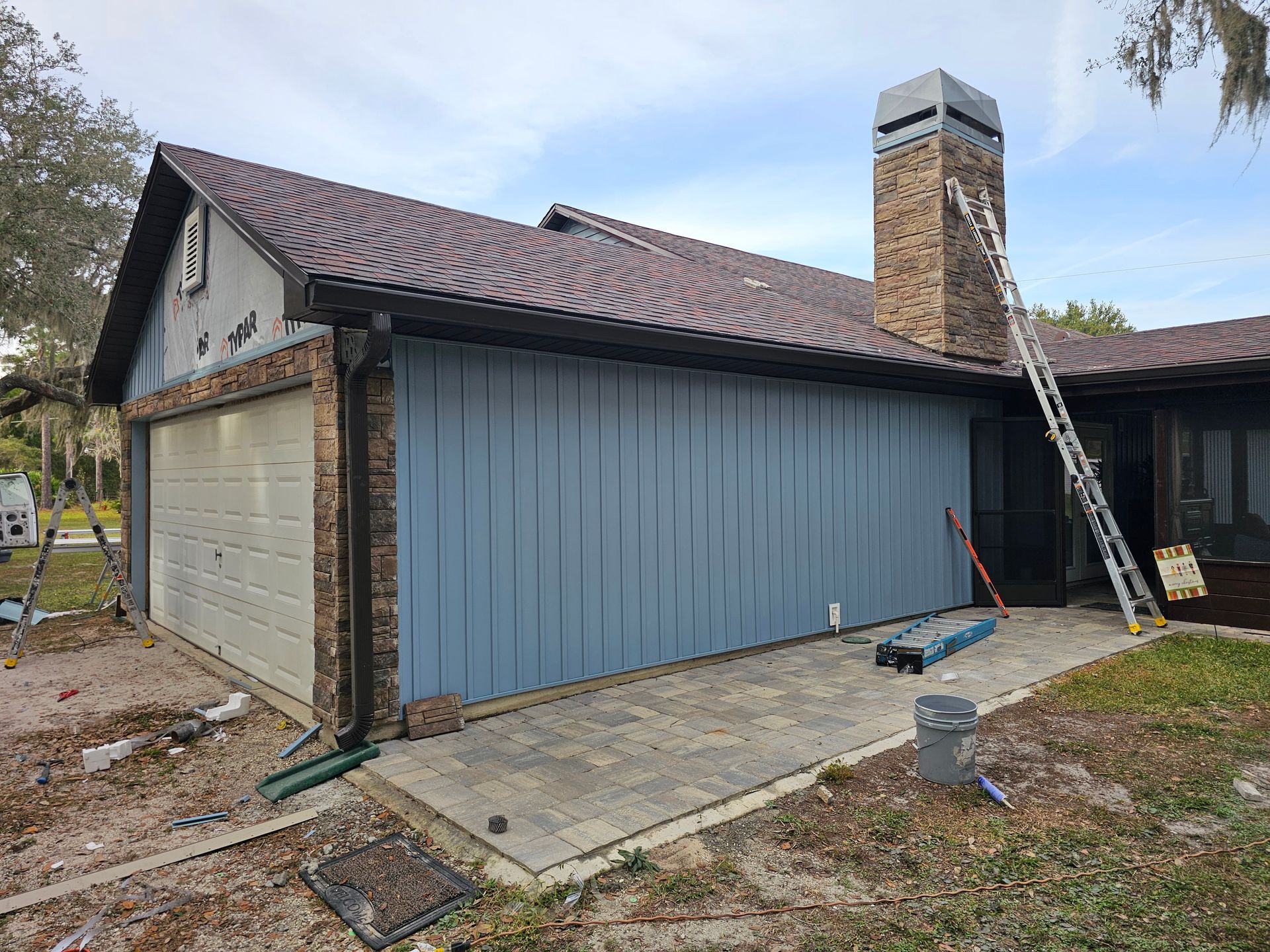 Exterior of a house with blue siding, a brick chimney, and a ladder leaning against the roofline