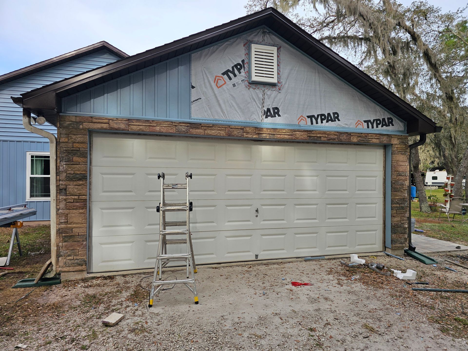 Garage under construction with ladder in front and exposed siding above the white door.