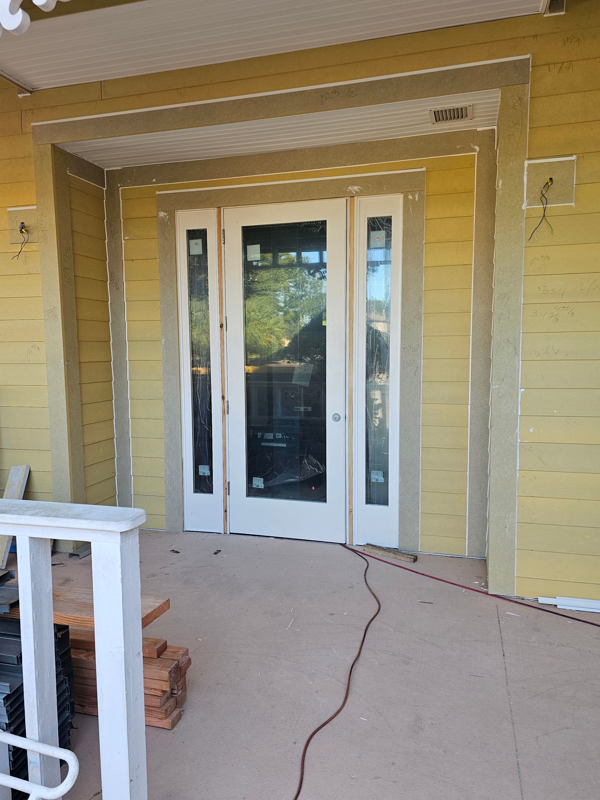 Front porch with white double glass doors, pale yellow siding, and a cable lying across the floor.