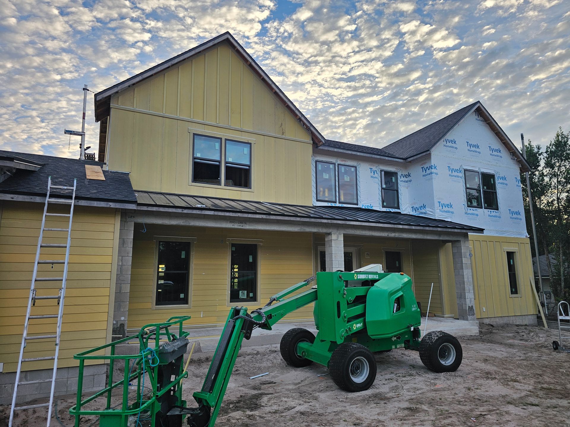 Green boom lift in front of a yellow and white house under construction at dusk