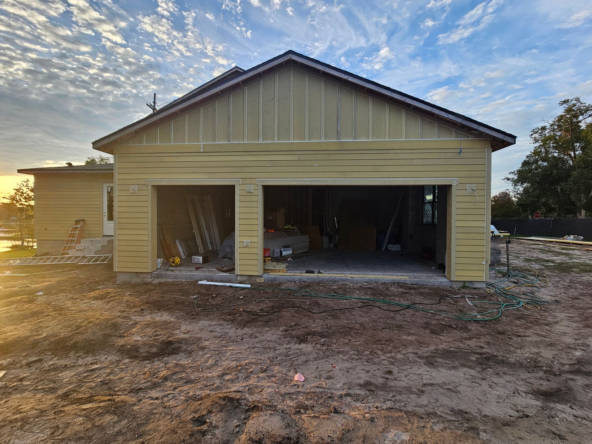 Partially built beige garage with open bays at sunset, dirt lot in front.