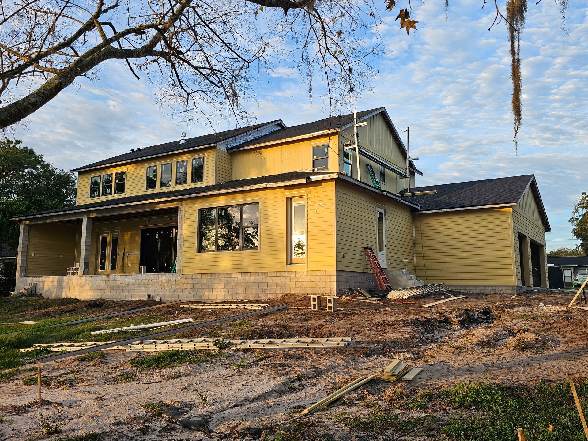 Two-story yellow house with damaged windows and a partially collapsed porch under a cloudy sky