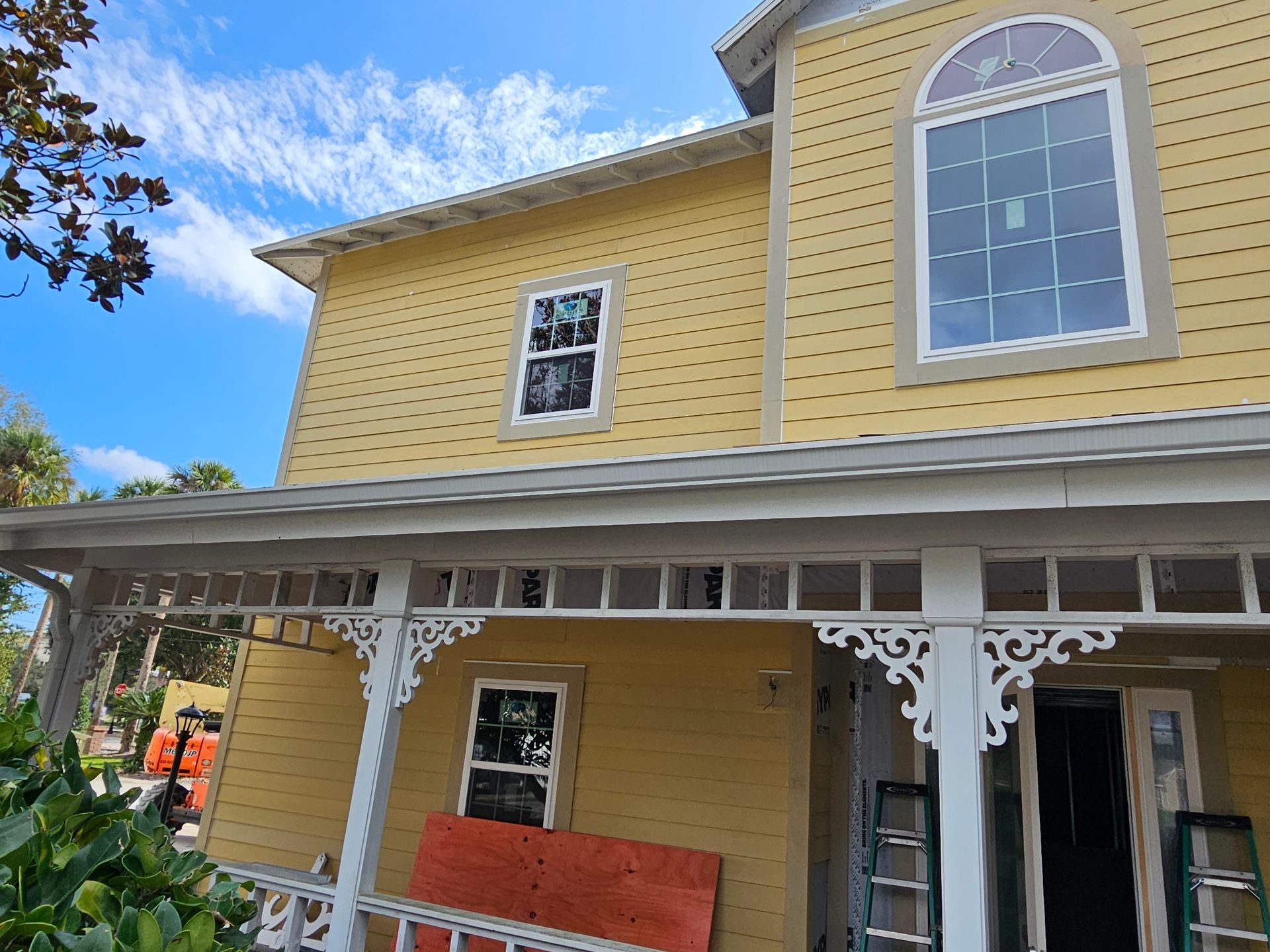 Yellow house with white trim and porch, viewed from below under a blue sky