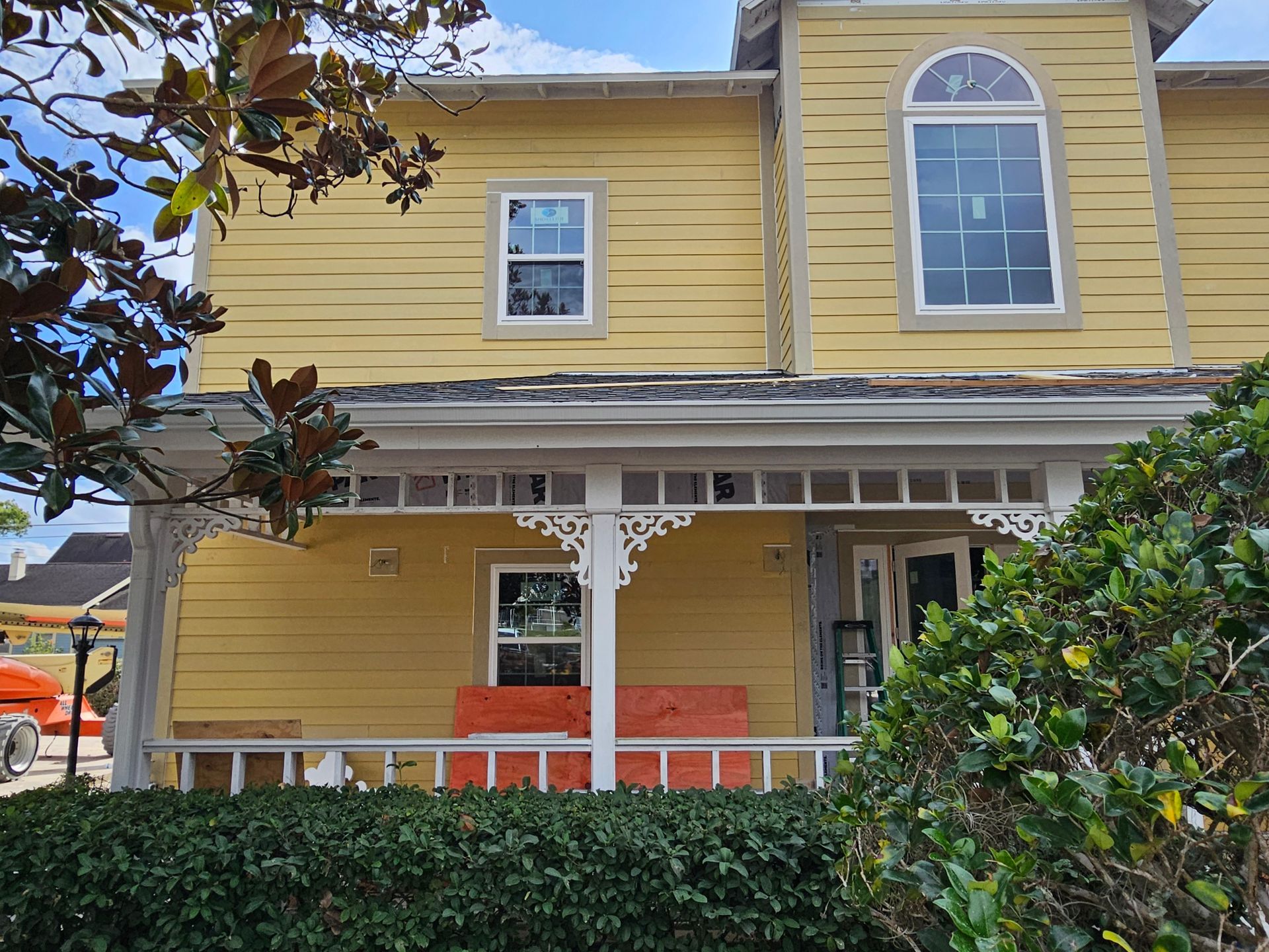 Yellow two-story house with white trim, porch, and green hedges in front