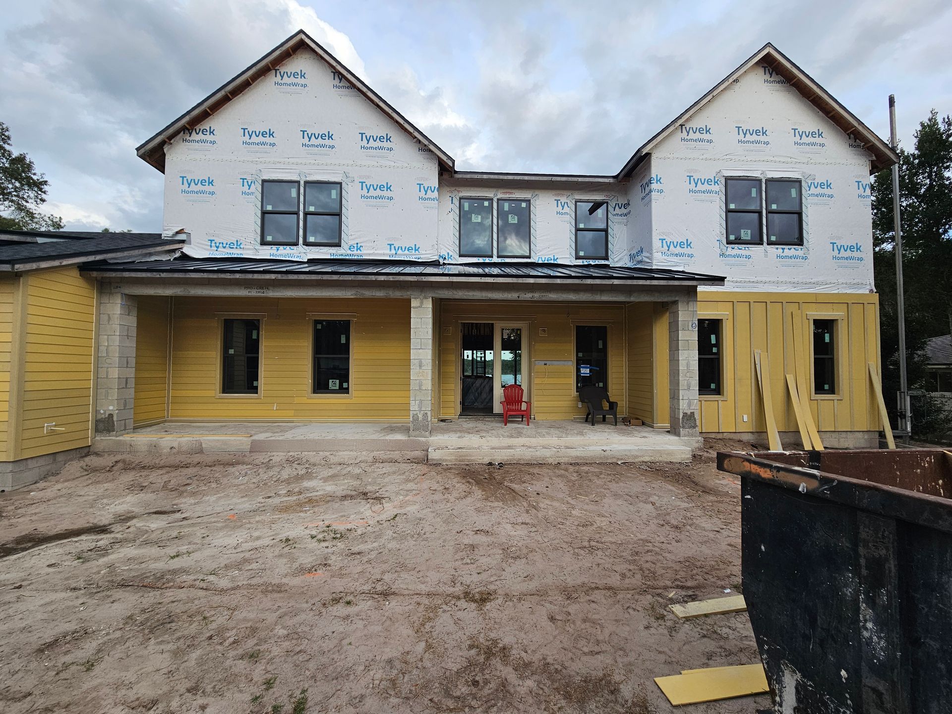 Two-story house under construction with yellow siding, exposed wrap, and muddy front yard