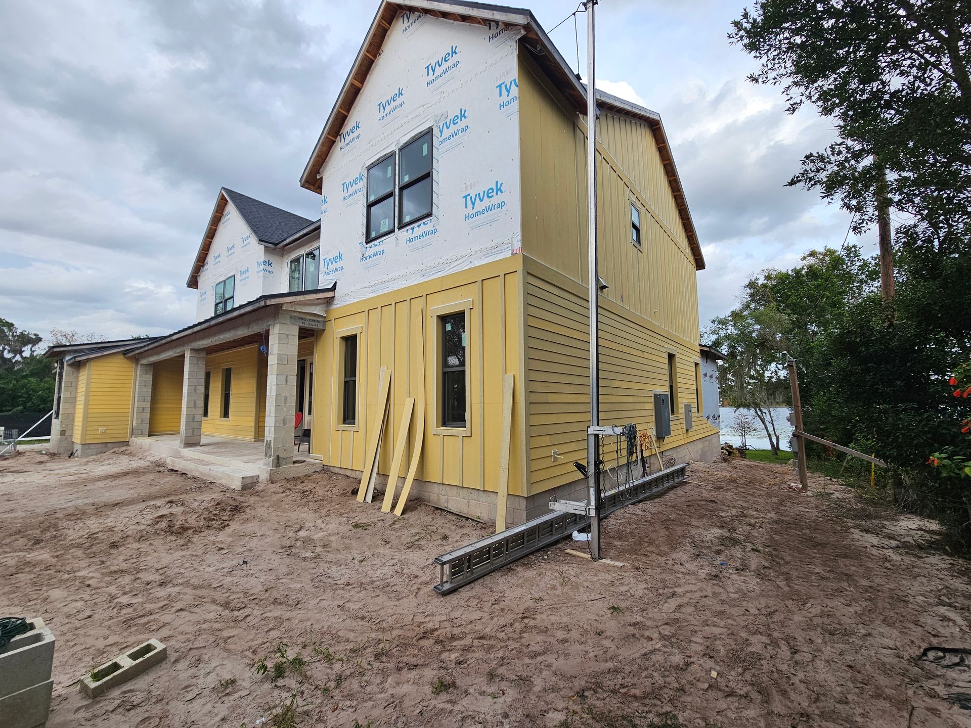 Two-story yellow house under construction with exposed wood framing and muddy ground