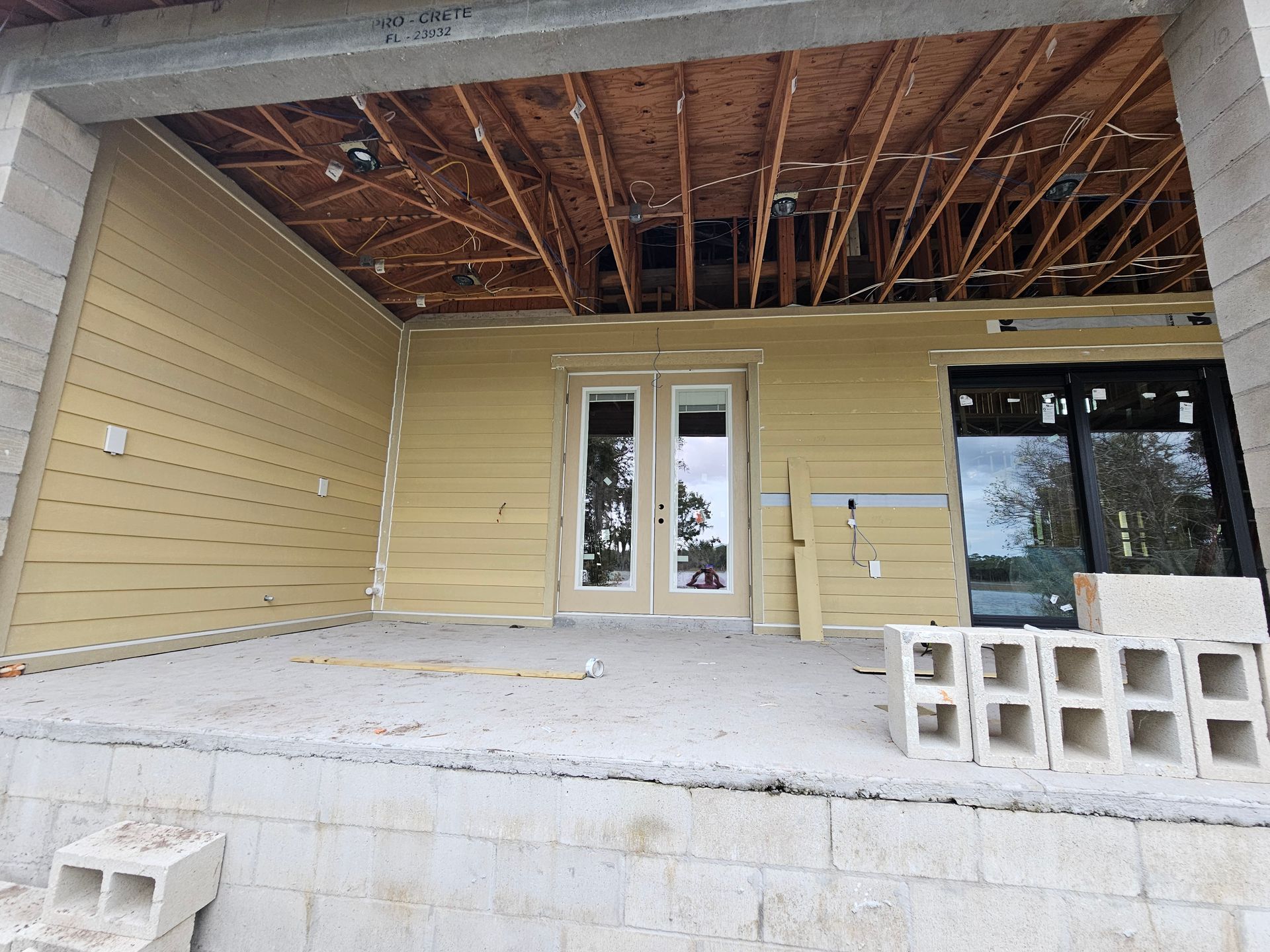 Partially built covered porch with cinder blocks, exposed rafters, and French doors on yellow siding