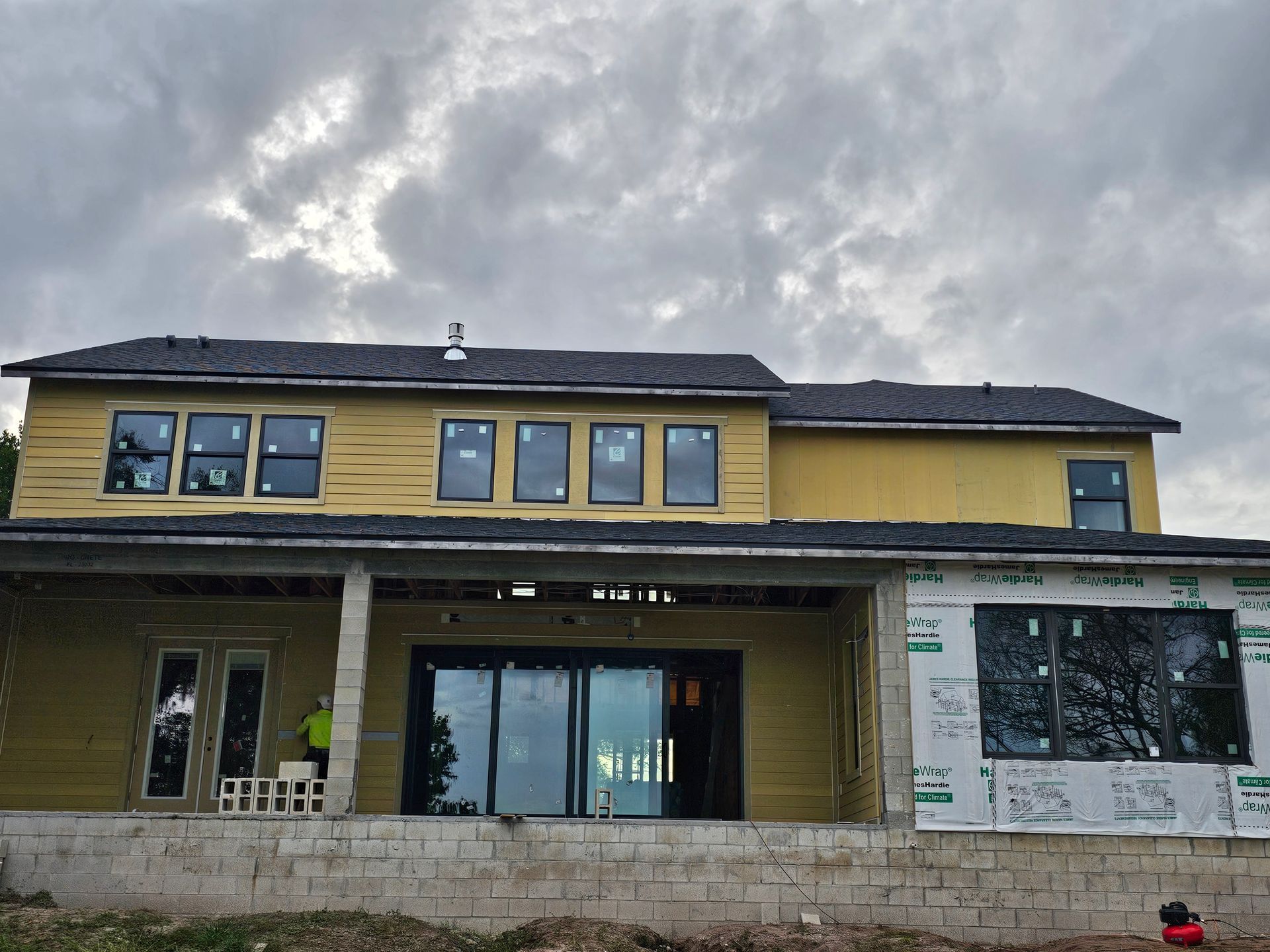 Two-story yellow house under construction with stone lower exterior and cloudy sky above