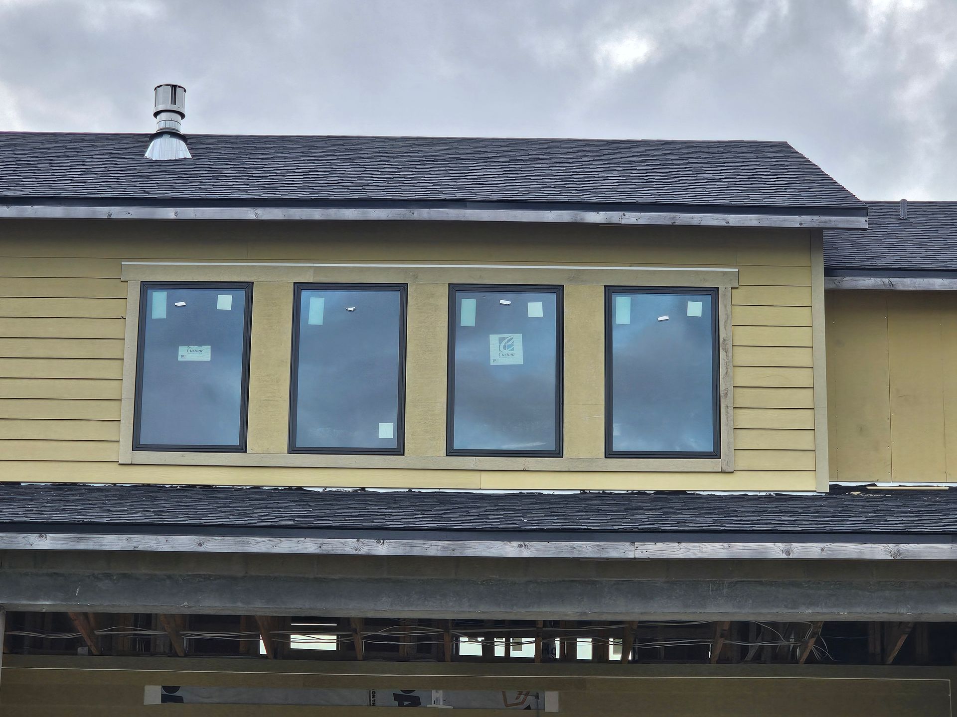Four blue-trimmed windows in a pale yellow house wall with exposed construction below