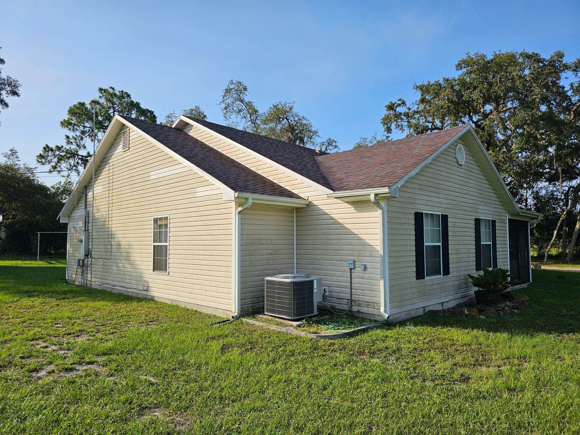 Single-story cream house with a red roof and black shutters on a grassy lot under a blue sky