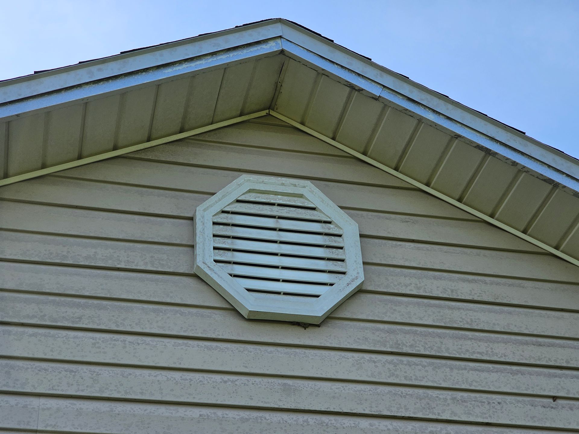 Octagonal attic vent on beige house siding beneath a blue roof gable